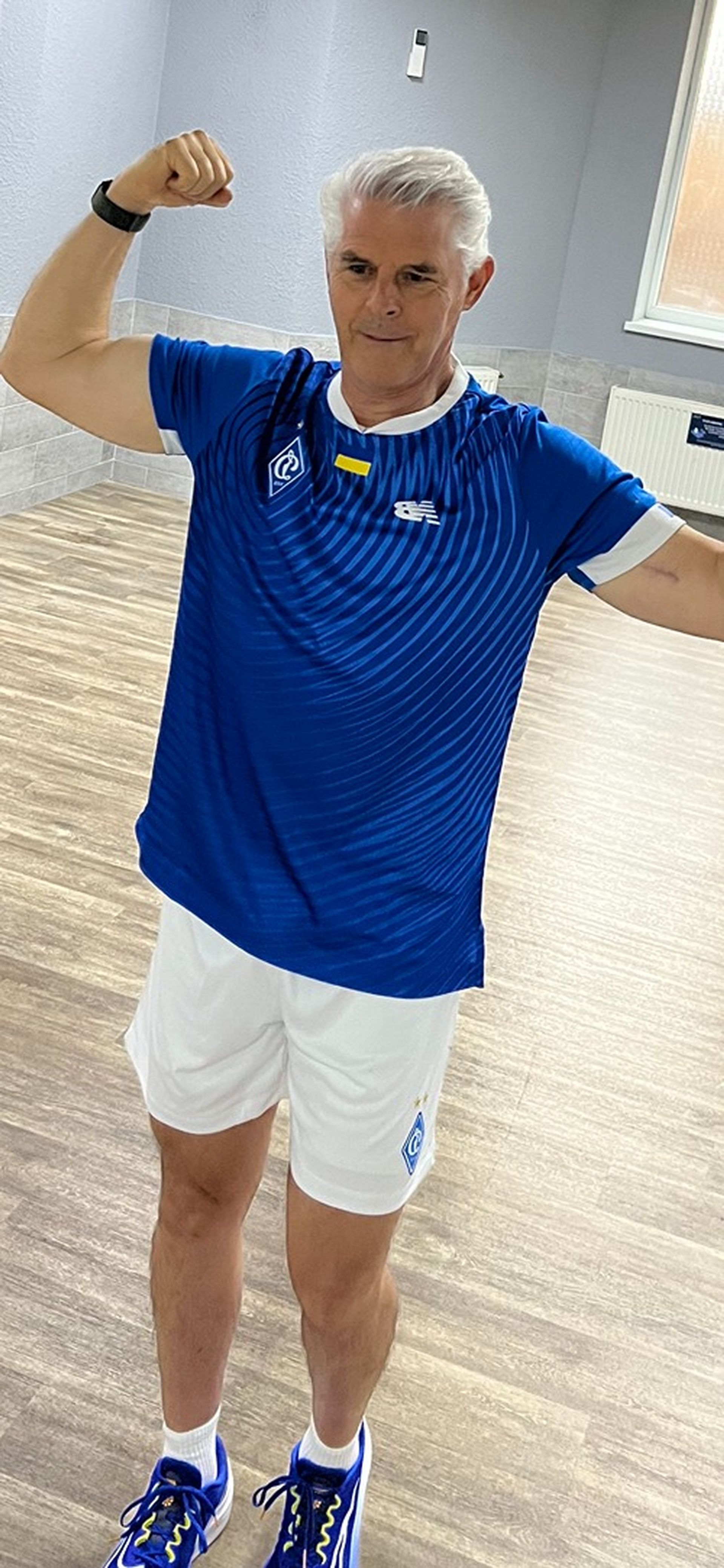 Tom Wright in a blue shirt and white shorts is flexing his muscles.