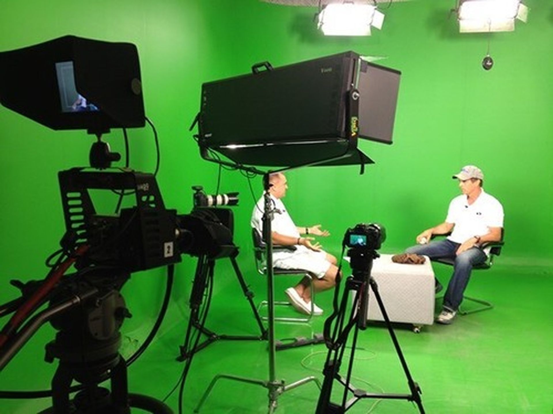 Two men are sitting in front of a green screen