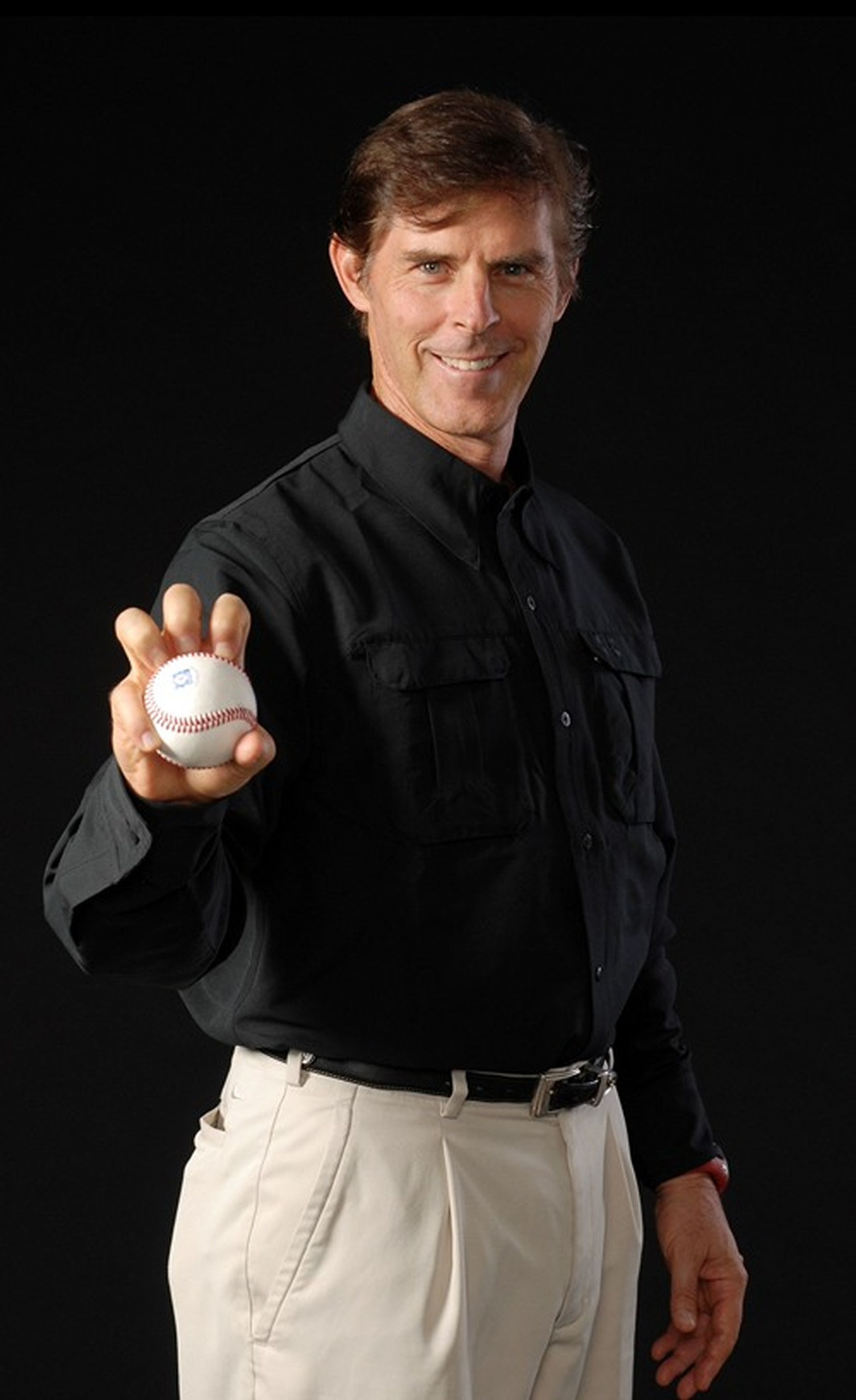 Tom Wright in a black shirt and white pants is holding a baseball.