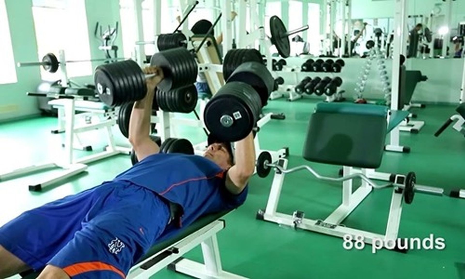 Tom Wright is lifting dumbbells on a bench in a gym.
