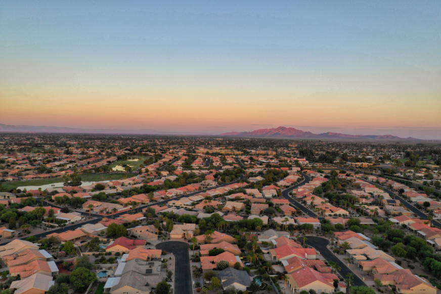 An aerial view of a residential area at sunset with mountains in the background.