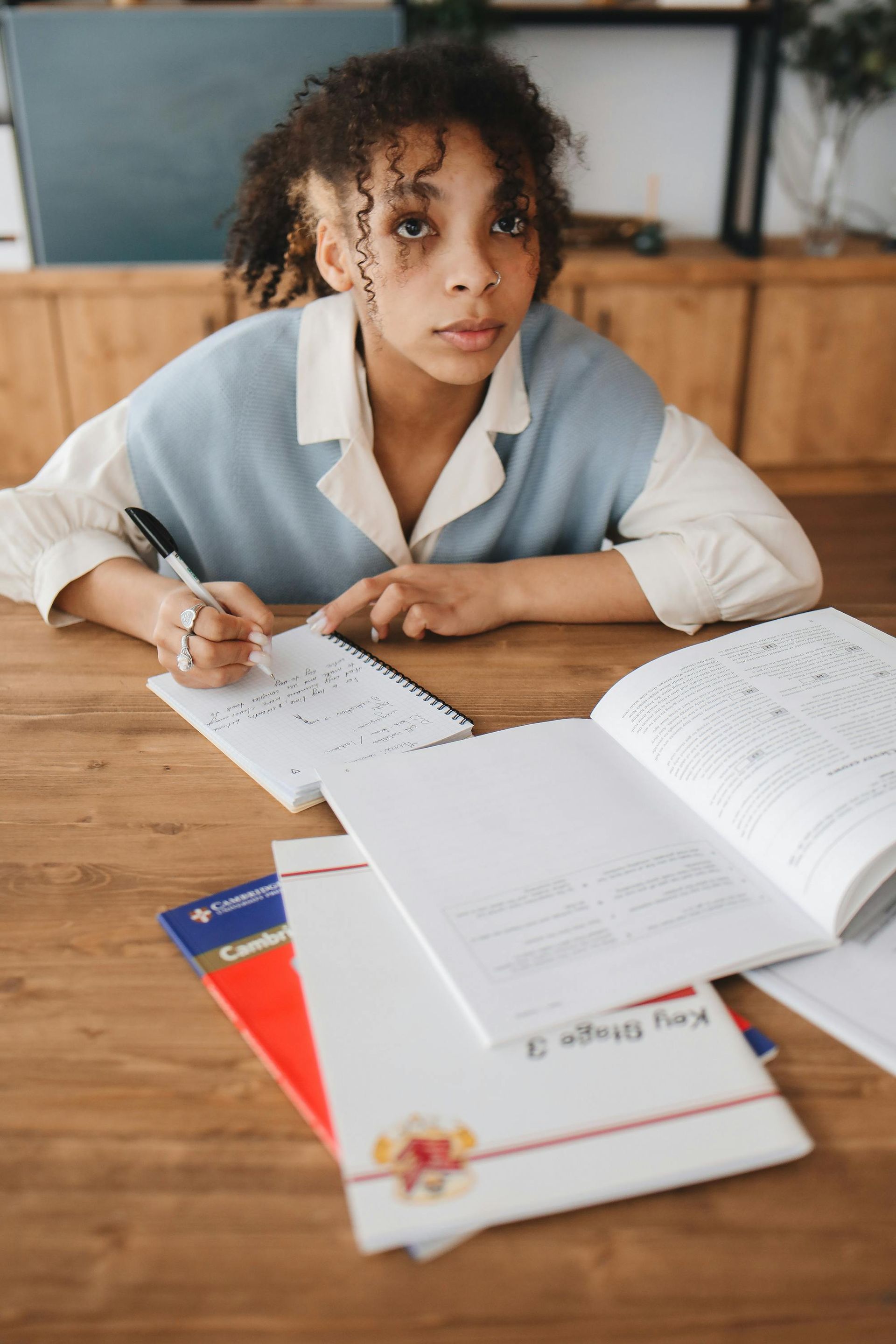 Young Black woman with dark hair and a black shirt, looking at the camera. She is against a peach-colored wall.