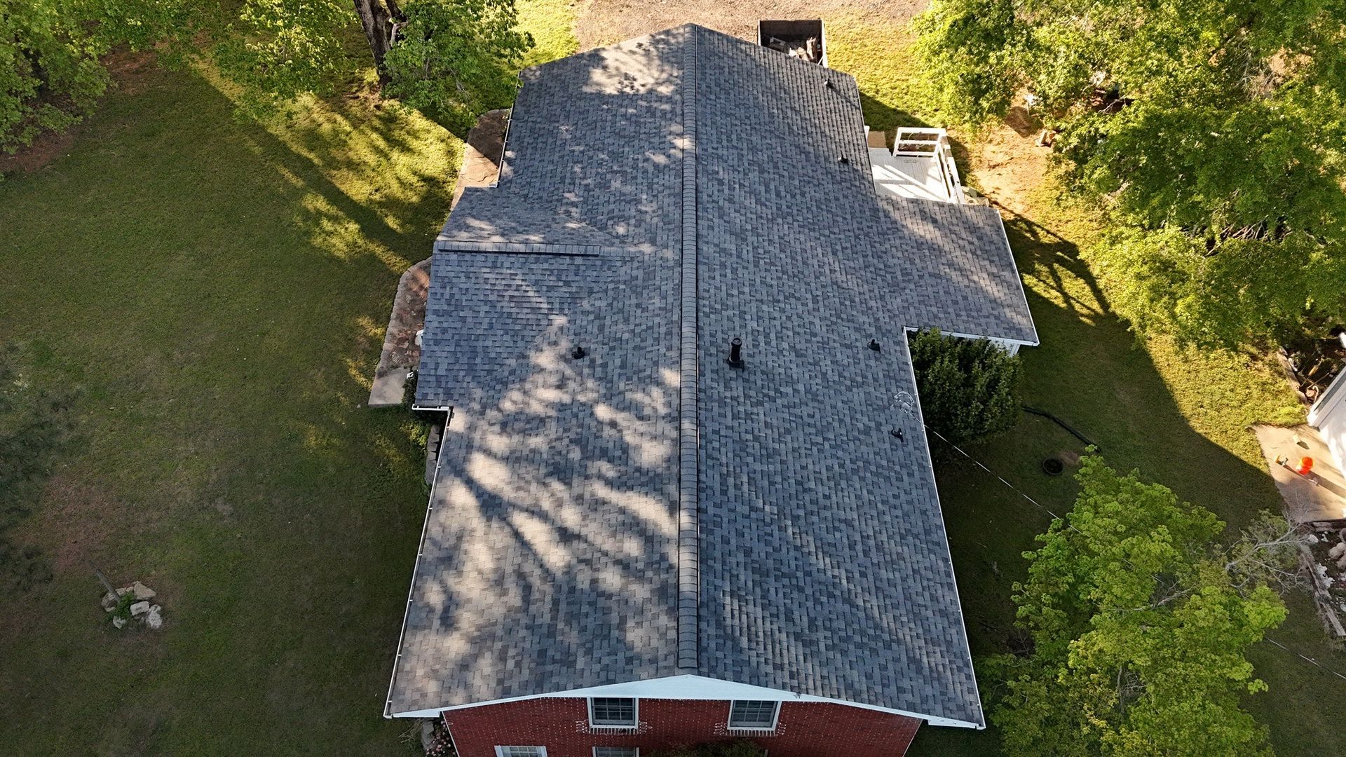 An aerial view of a house with a new roof surrounded by trees.