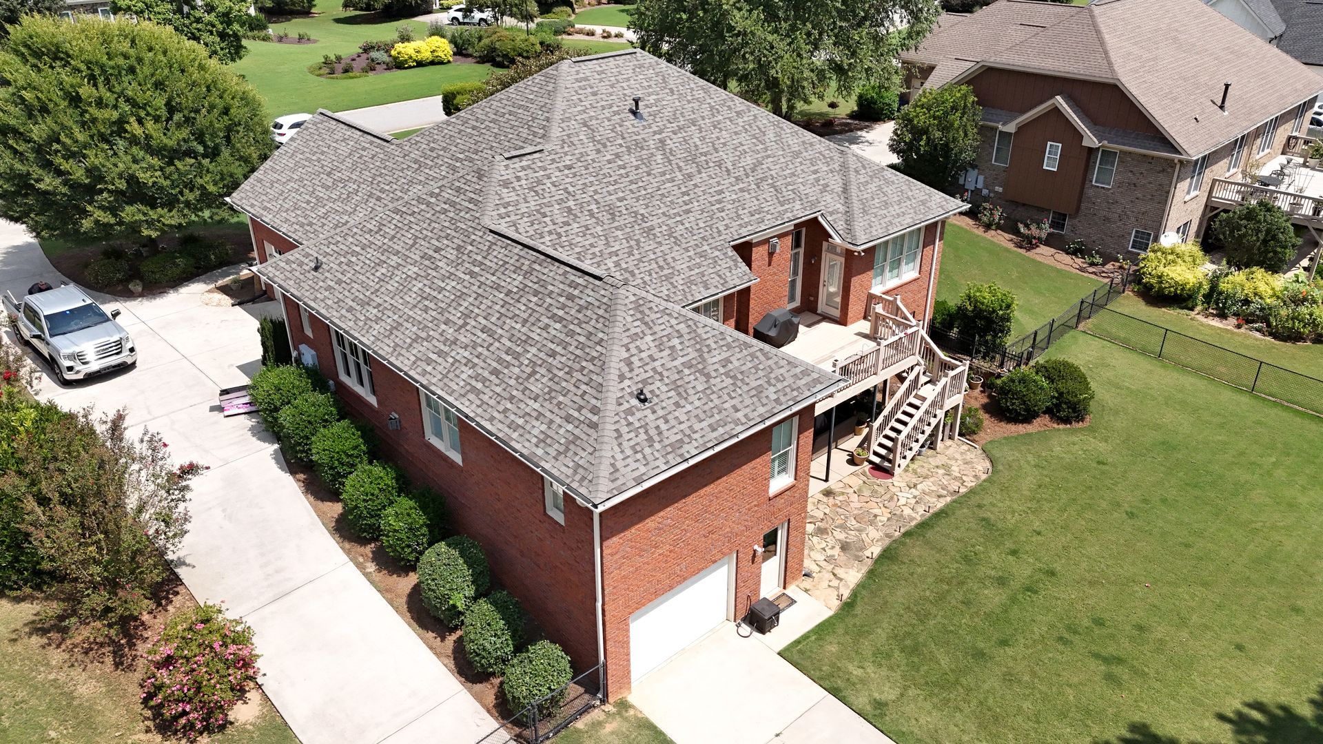 An aerial view of a large brick house with a gray roof in a residential neighborhood.