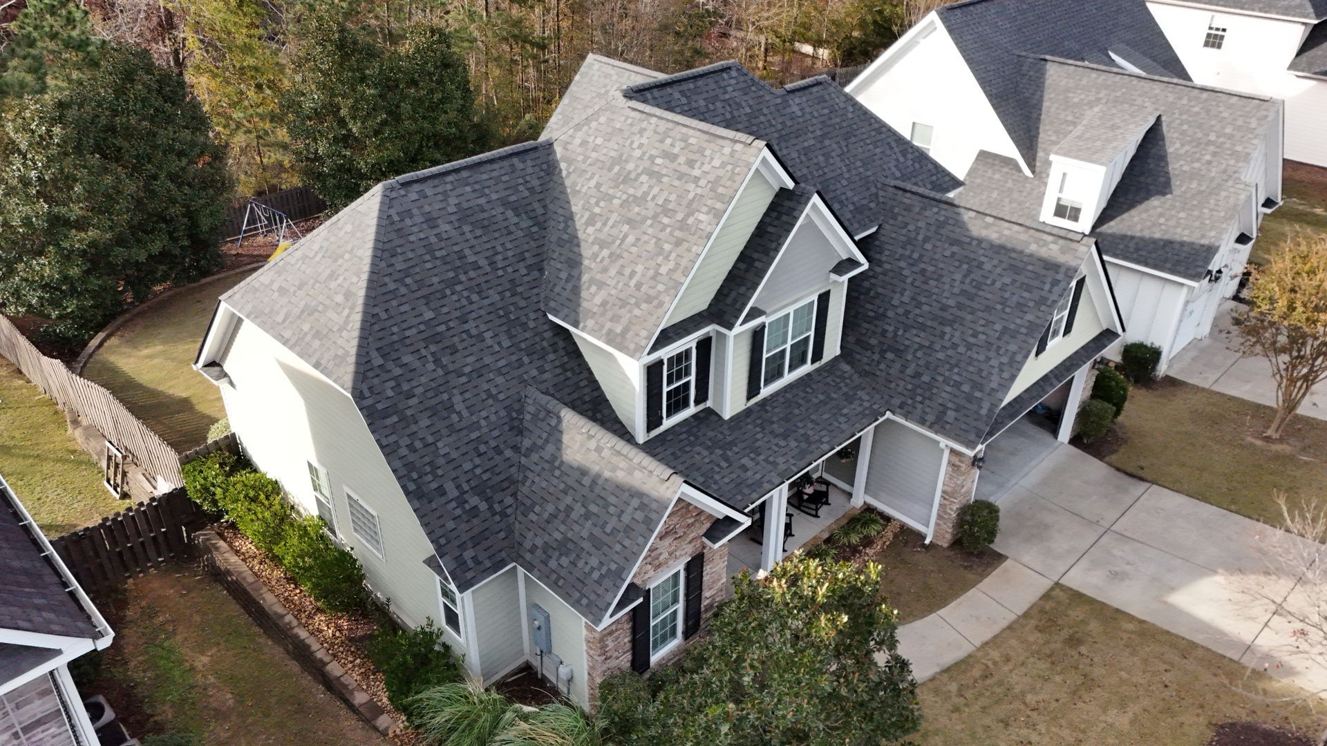 An aerial view of a large white house with a black roof in a residential area.