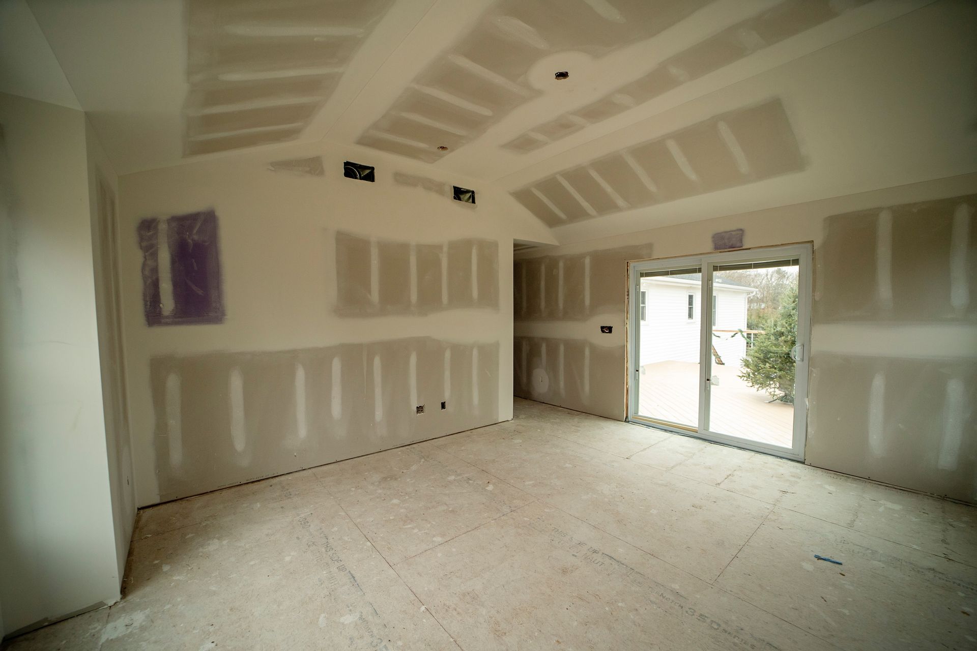 An empty room with drywall and a sliding glass door