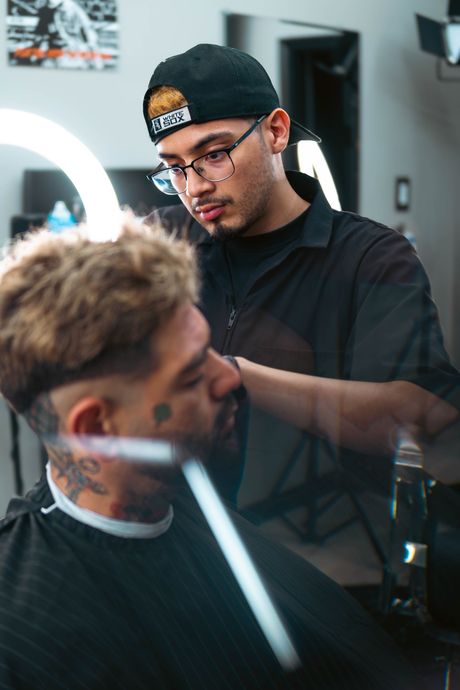 A barber carefully styles a client's hair in a professional, brightly lit salon setting.  The Studio Barbershop