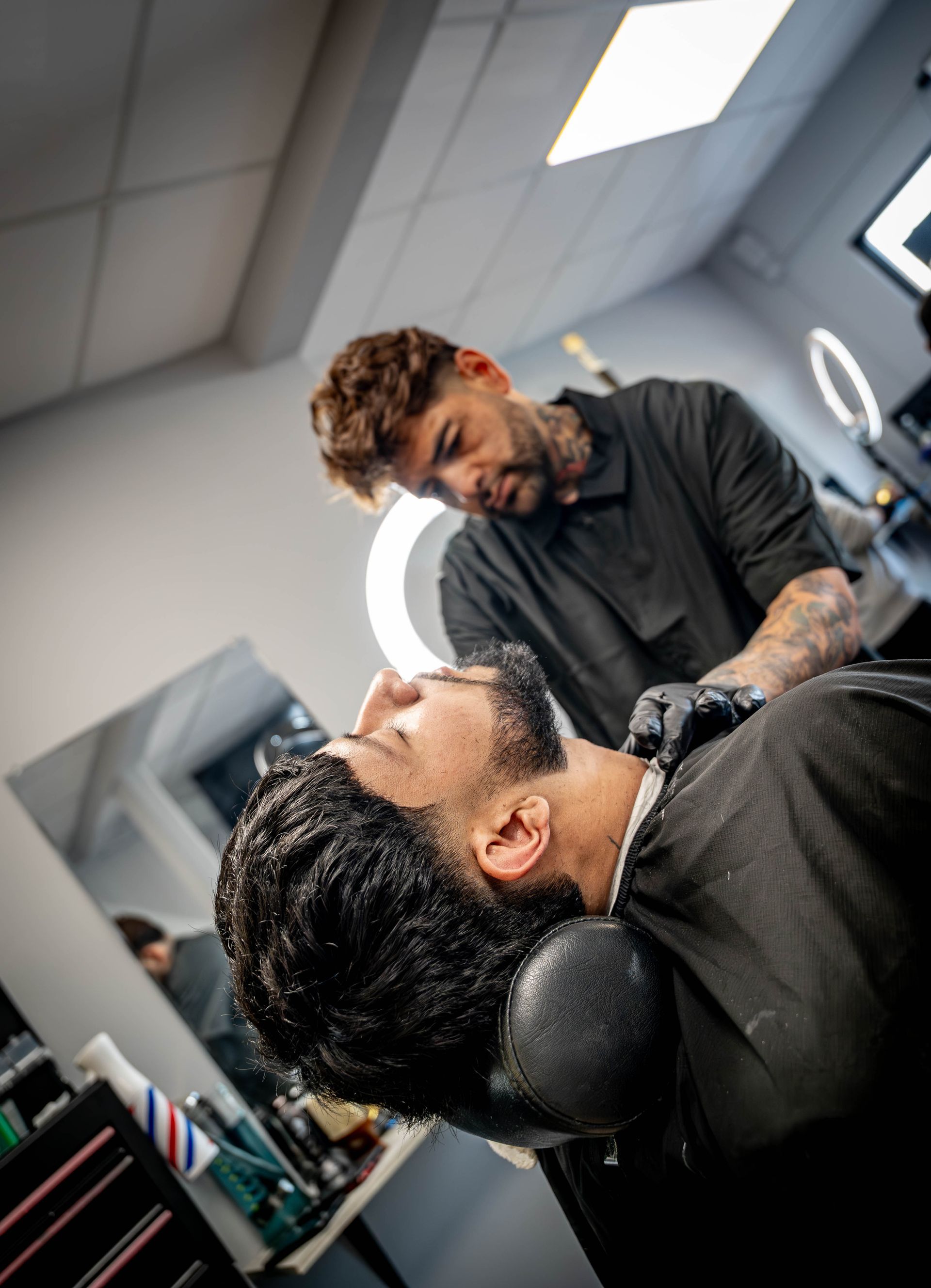 A barber wearing black gloves performs a professional shave on a client reclining in a salon chair.