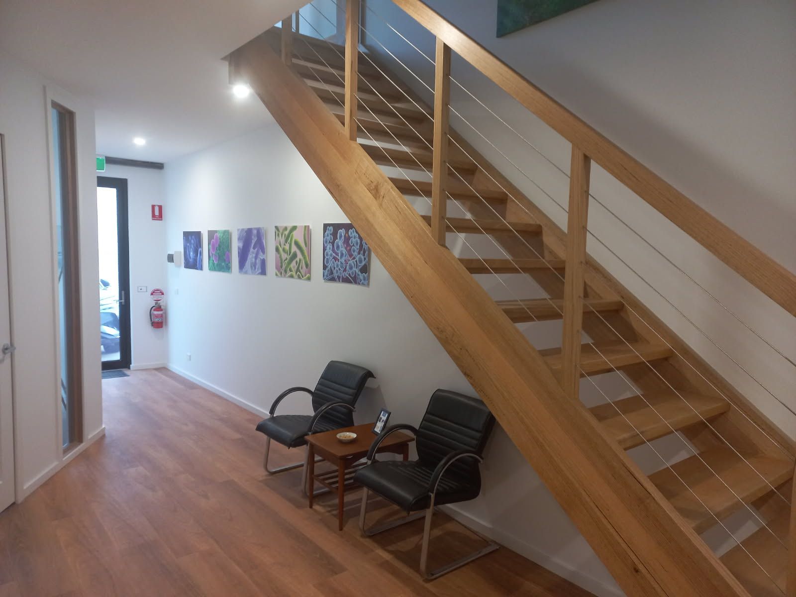 Hallway with wooden stairs, two black chairs, and artwork on the wall.