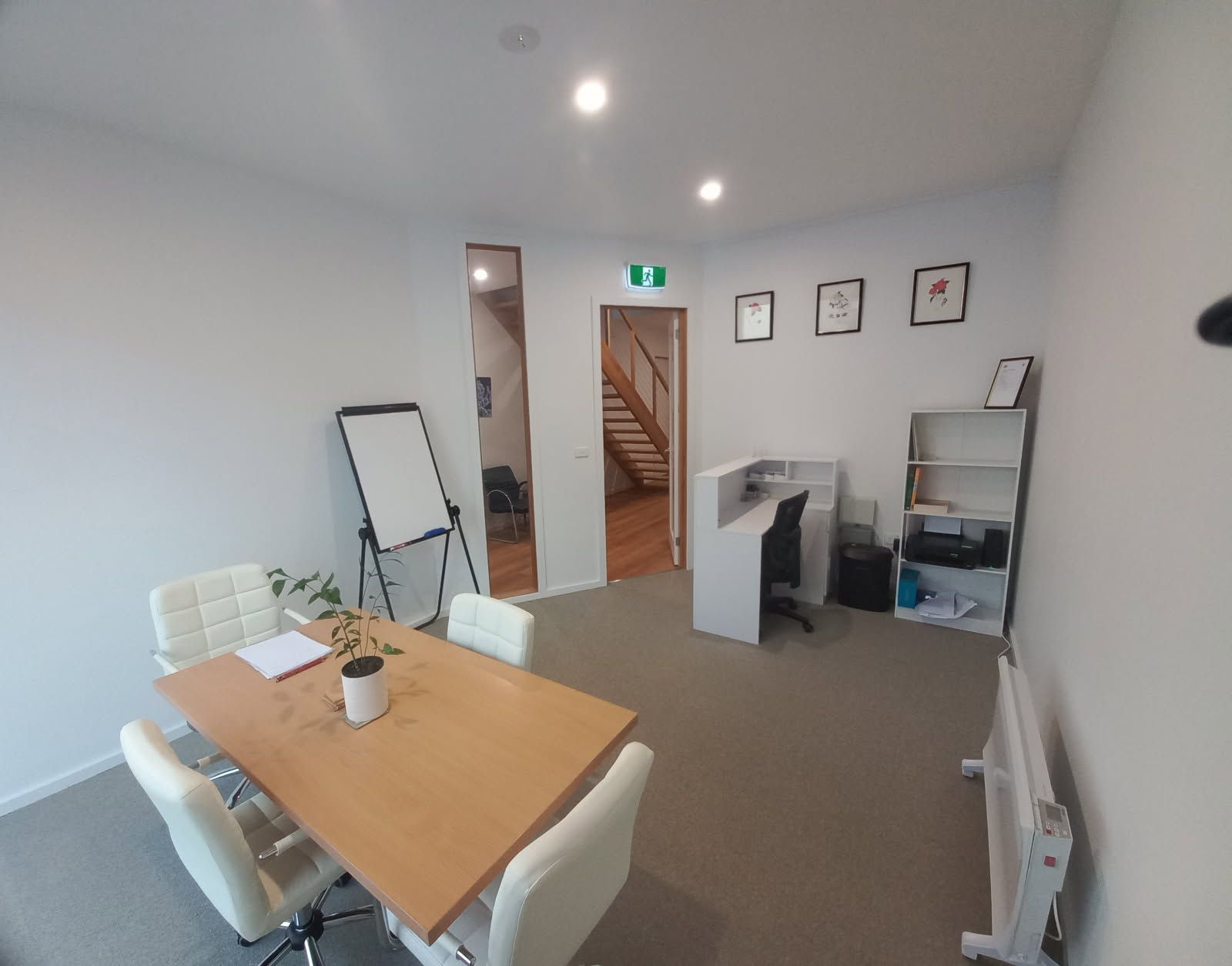 An office room with a table, chairs, and a whiteboard. There's a reception desk and a door leading to stairs.