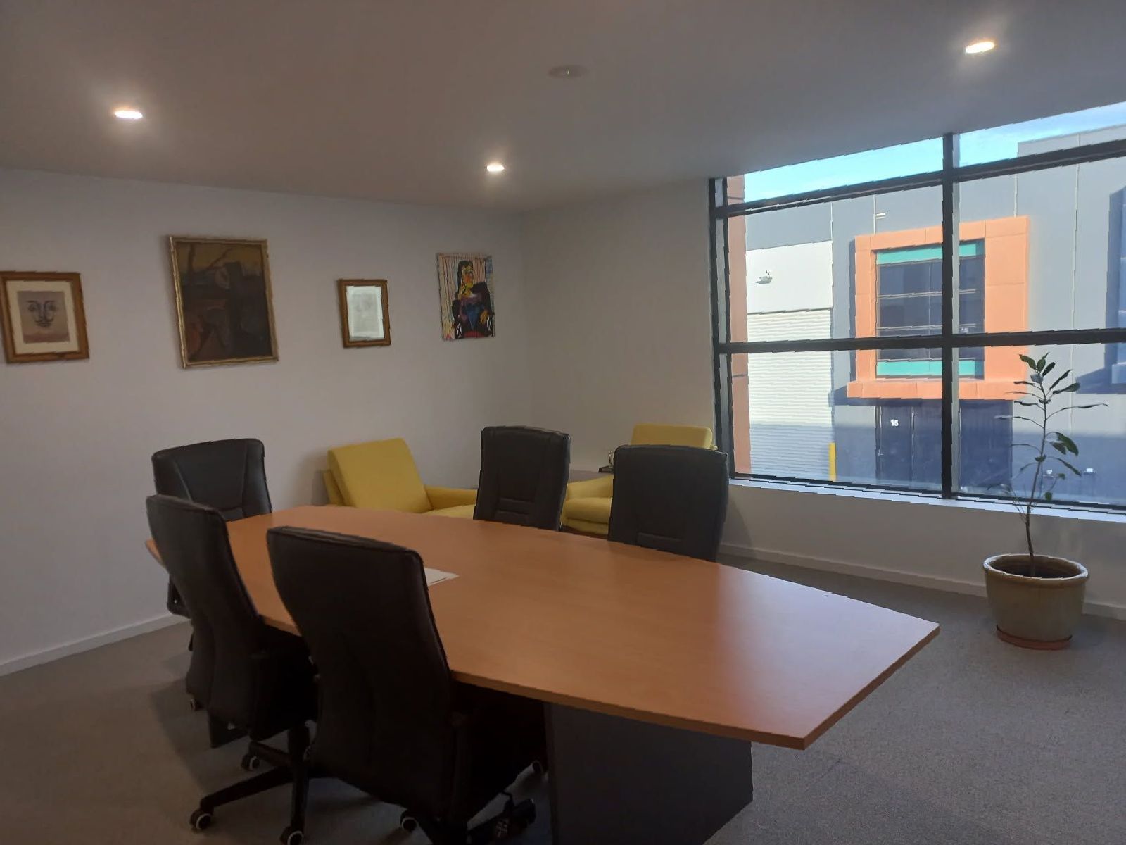 A conference room with a large table, chairs, artwork on the wall, and a large window overlooking a modern building.