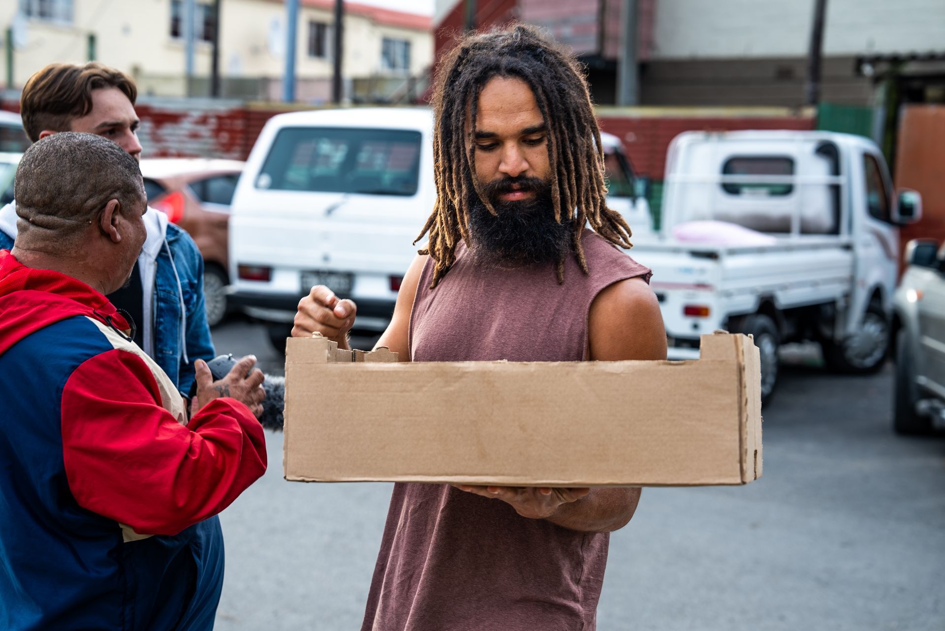 A man with dreadlocks is holding a cardboard box in his hands.