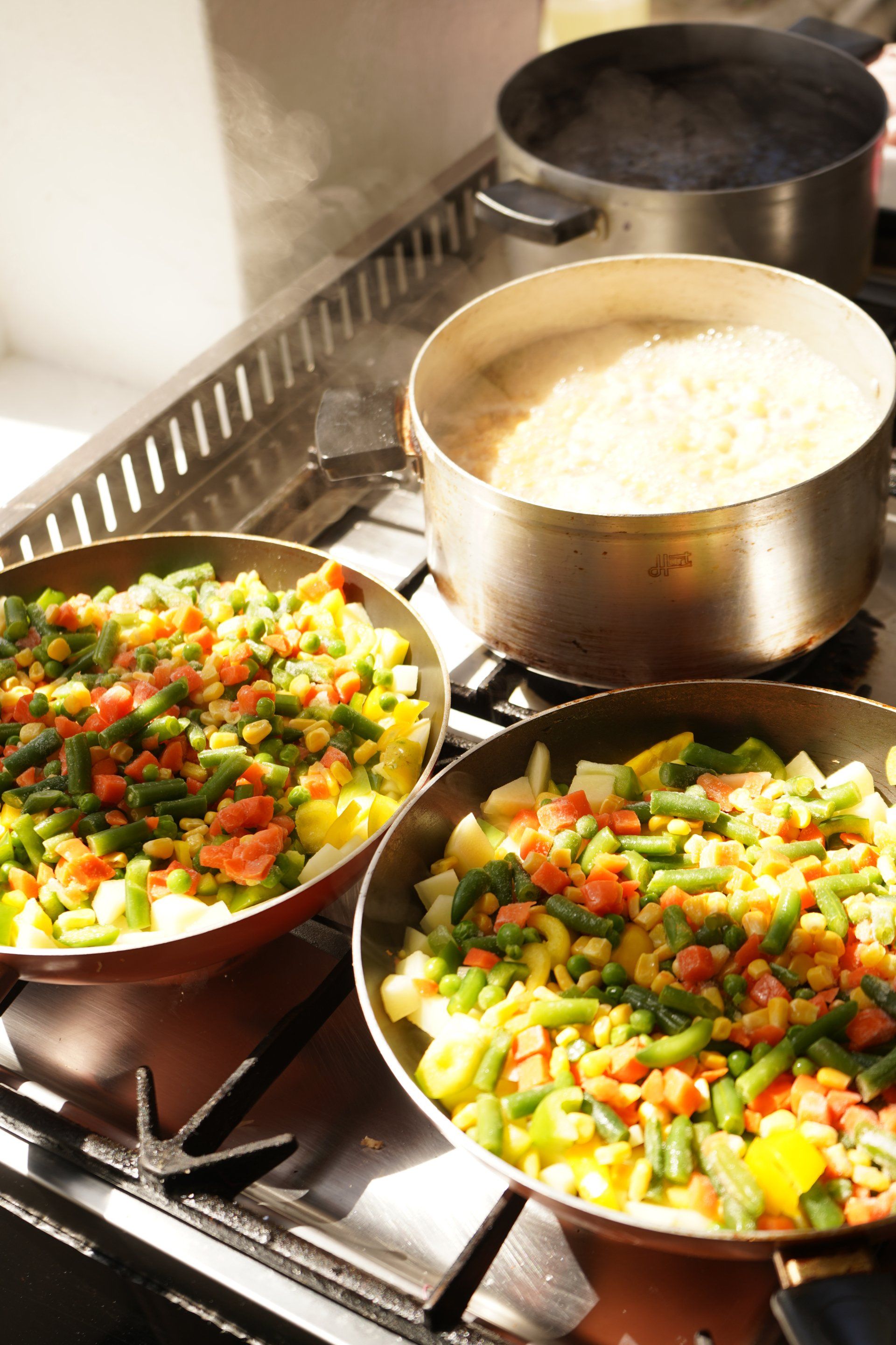 Two pans filled with vegetables are cooking on a stove