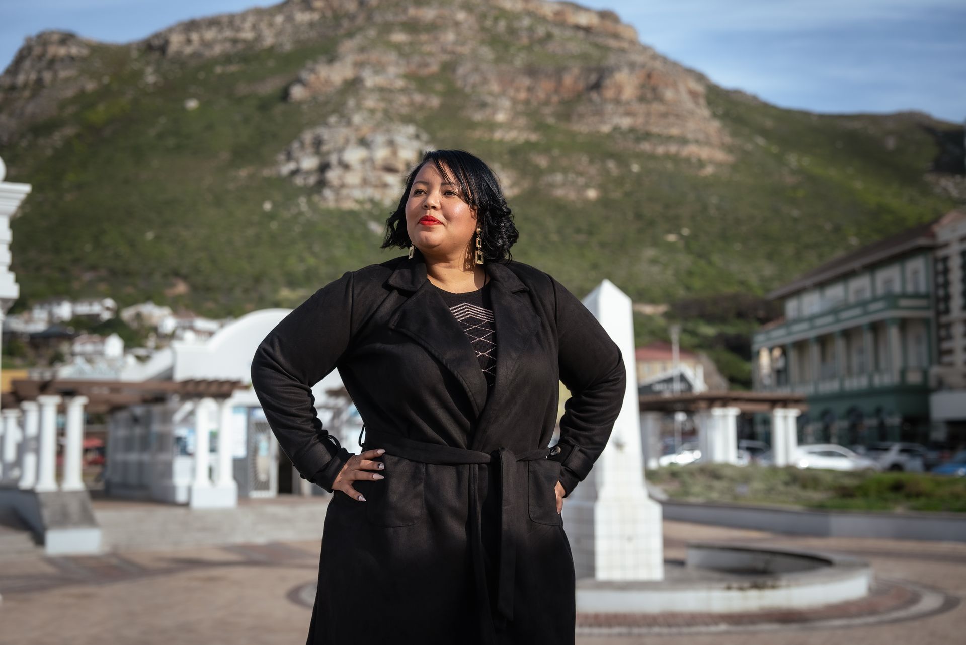 A woman in a black coat is standing in front of a mountain.