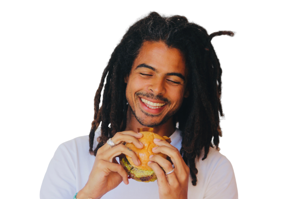 A man with dreadlocks is smiling while eating a hamburger
