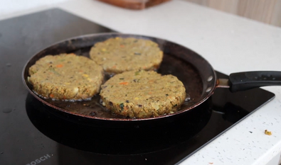 Three hamburger patties are cooking in a frying pan on a stove.