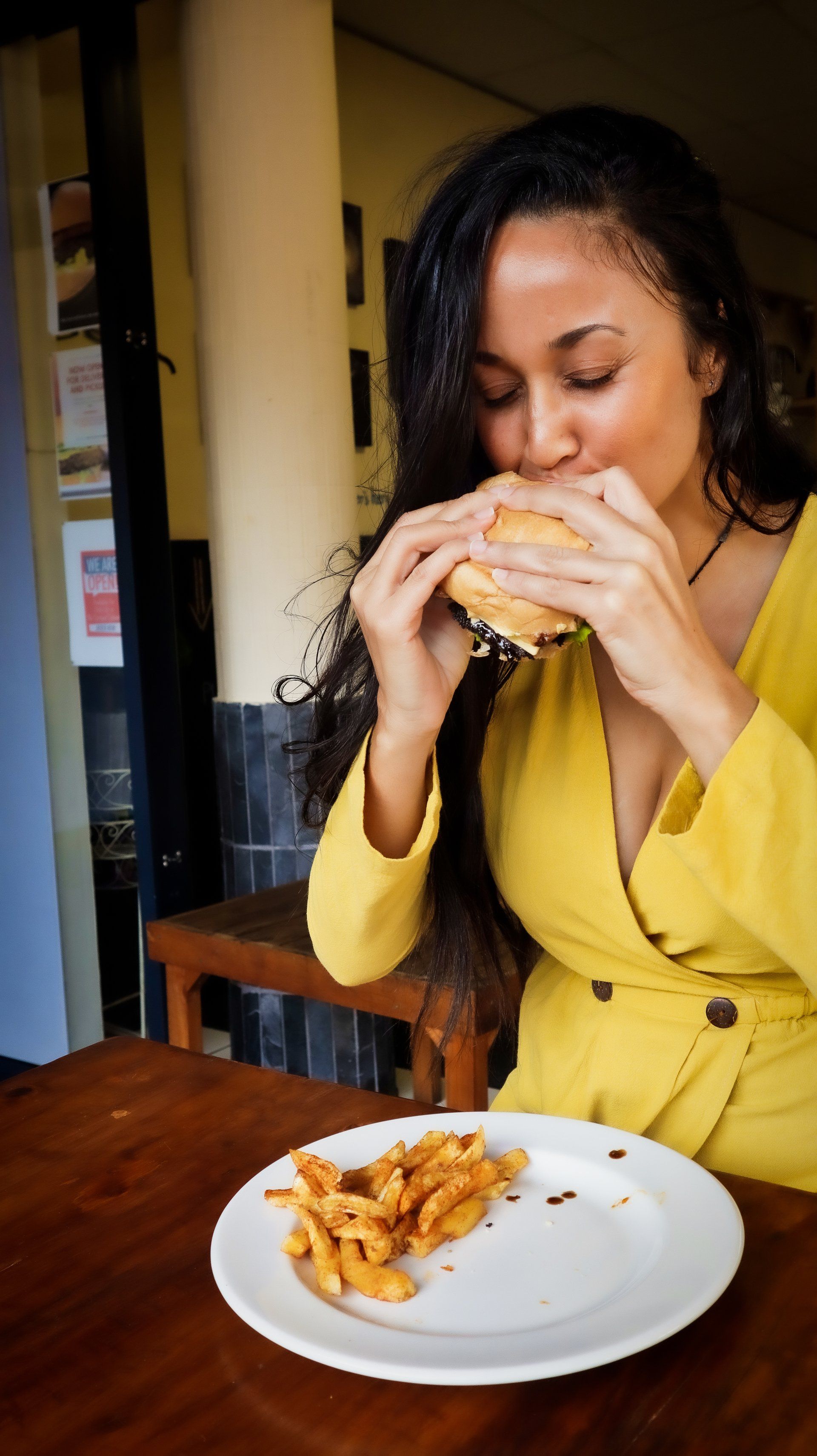 A woman is sitting at a table eating a hamburger and french fries.