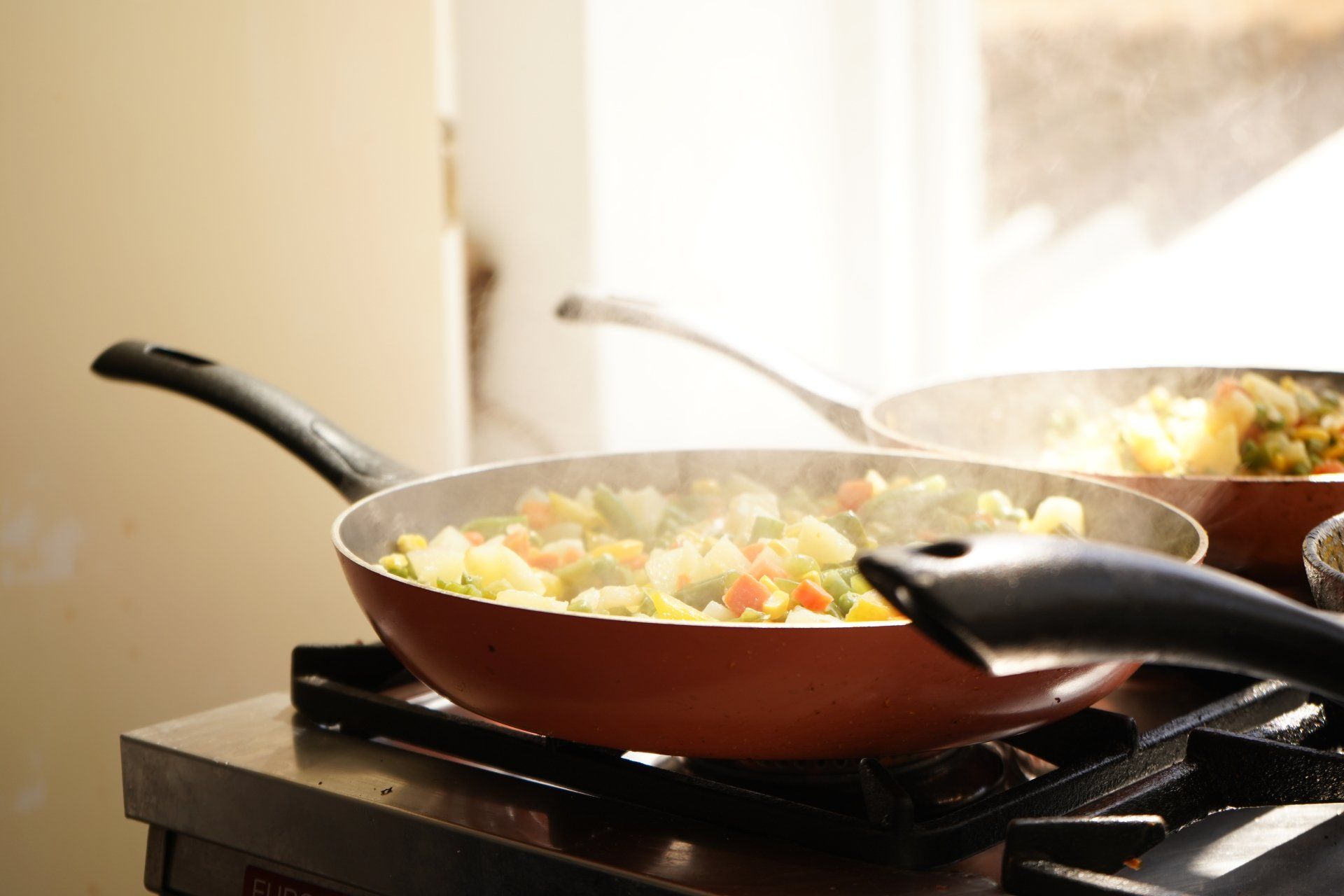 Two frying pans filled with vegetables are cooking on a stove.