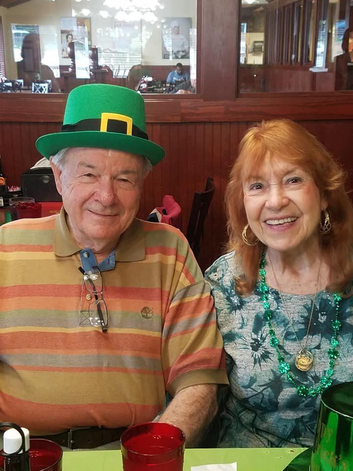 A man and a woman are sitting at a table in a restaurant . the man is wearing a leprechaun hat.