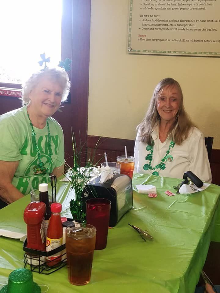 Two women are sitting at a table with a green table cloth.