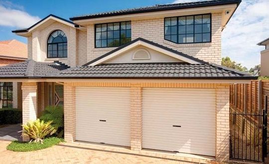 Large White Brick House With Two Garage Doors and a Black Roof — Coffs Garage Doors & Motors in Coffs Harbour, NSW