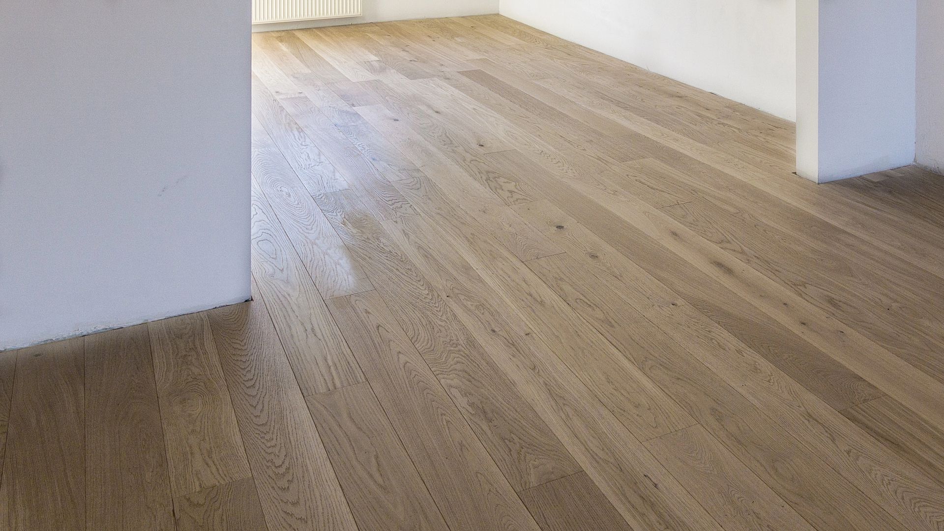 Pavimento in legno in una stanza con pareti bianche, prospettiva angolata.