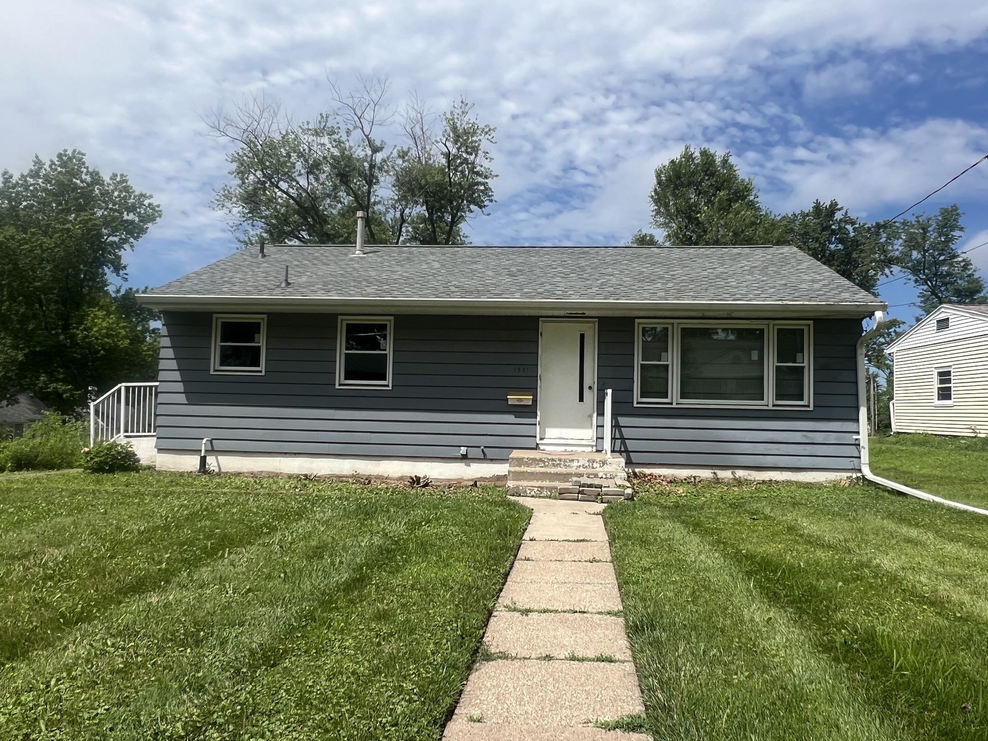 Single-story house with gray blue siding and a concrete path leading to the white front door.