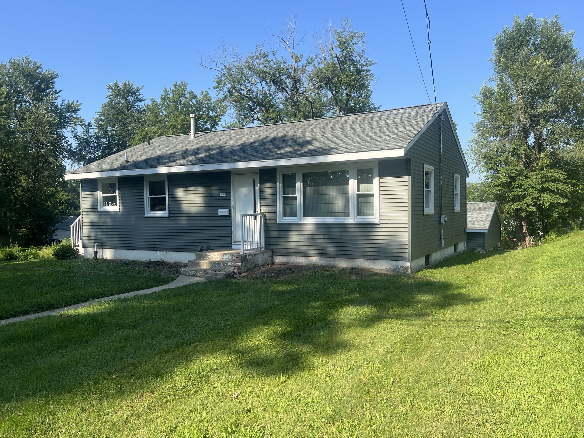 A house with gray blue siding and white trim and a green lawn under a blue sky.