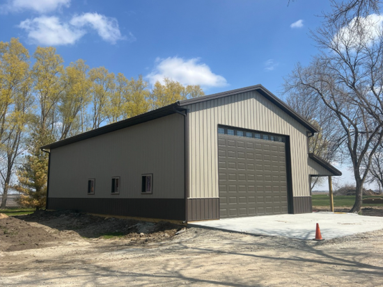 A large metal building with a large garage door is sitting in the middle of a dirt field.