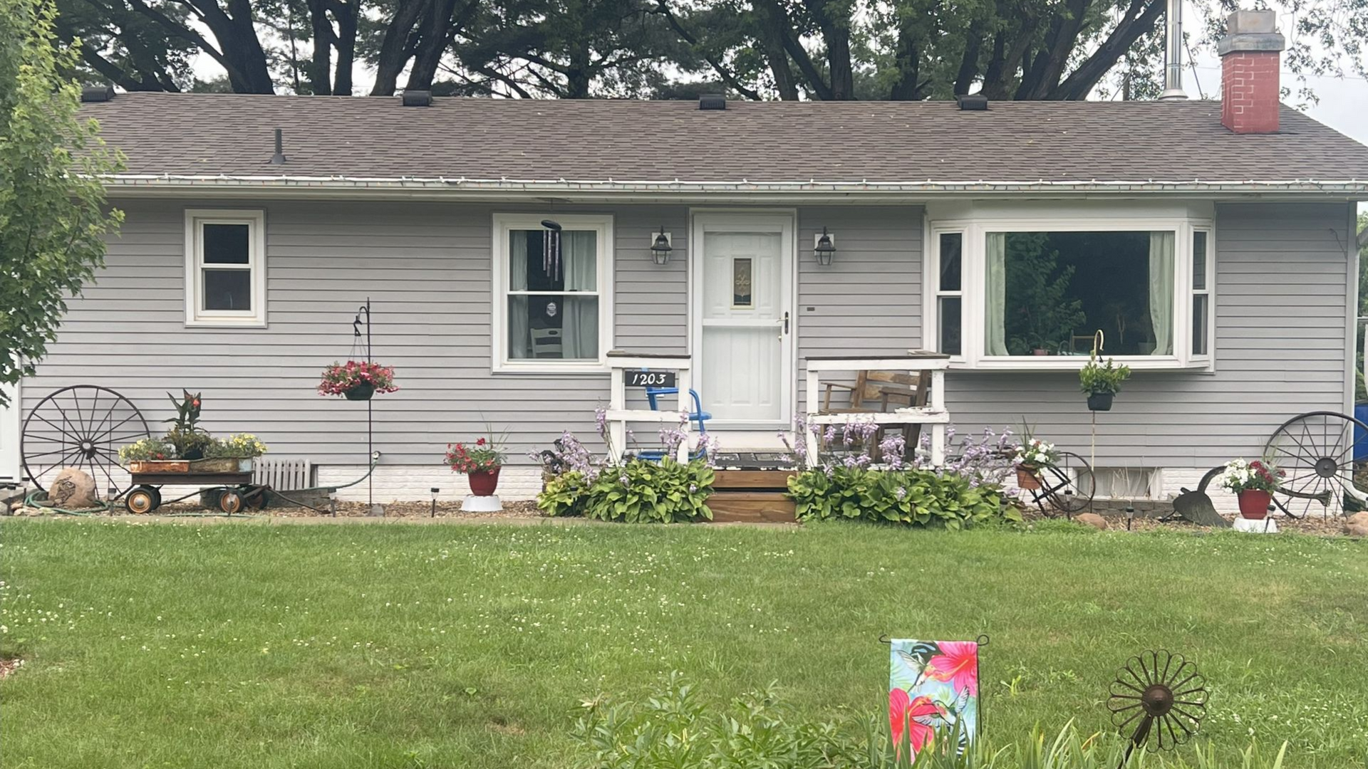 Gray house with a green lawn, flowers, and a bay window in Center Point, Iowa.