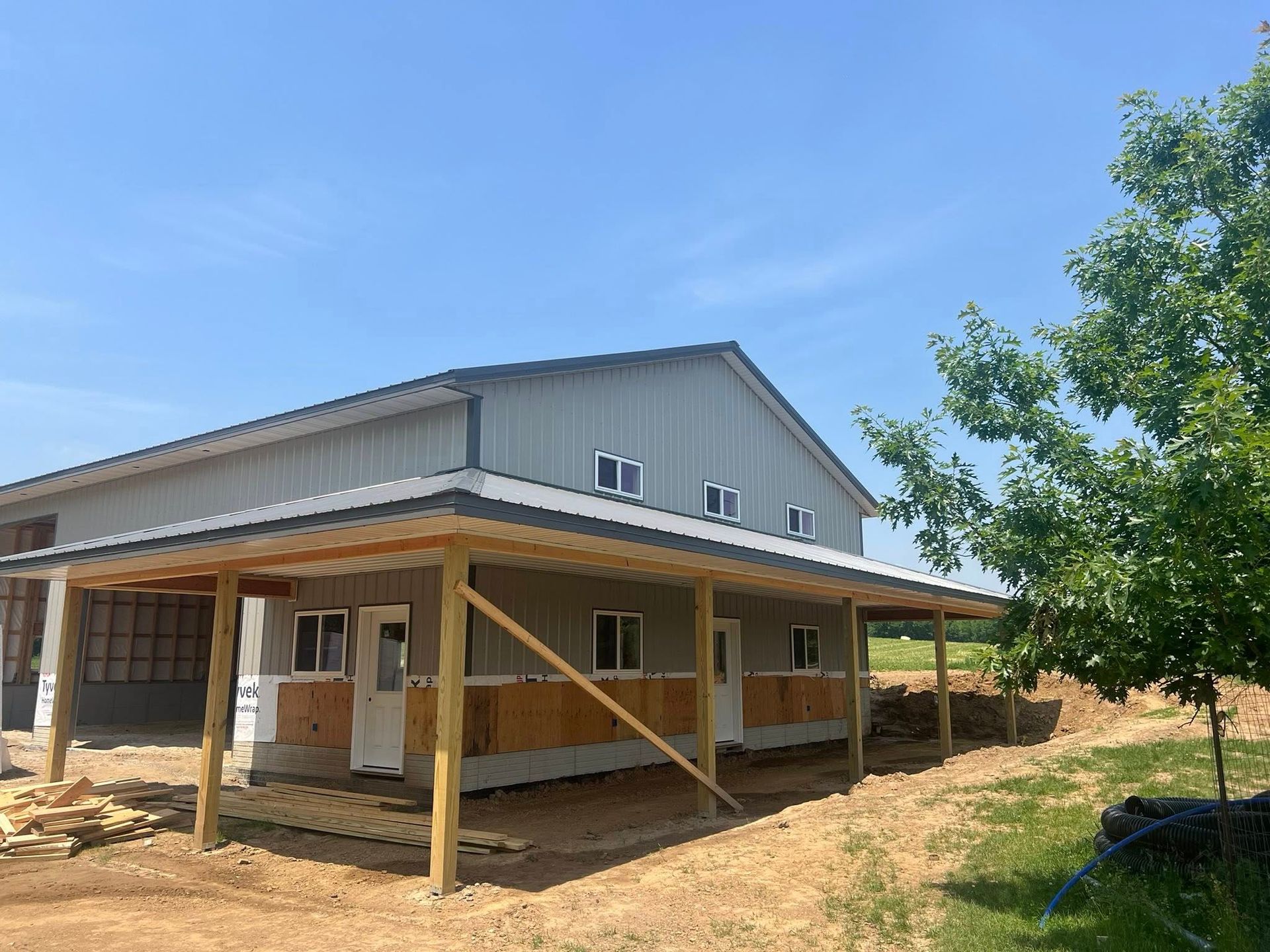 A pole barn under construction with a porch and a tree in front of it