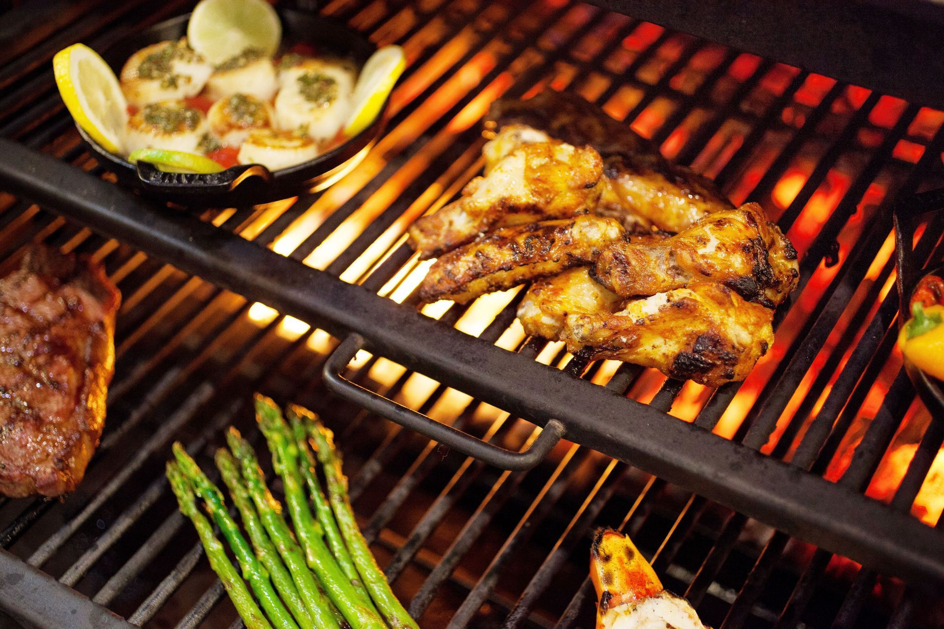 A grill with steaks , asparagus , and other food on it.