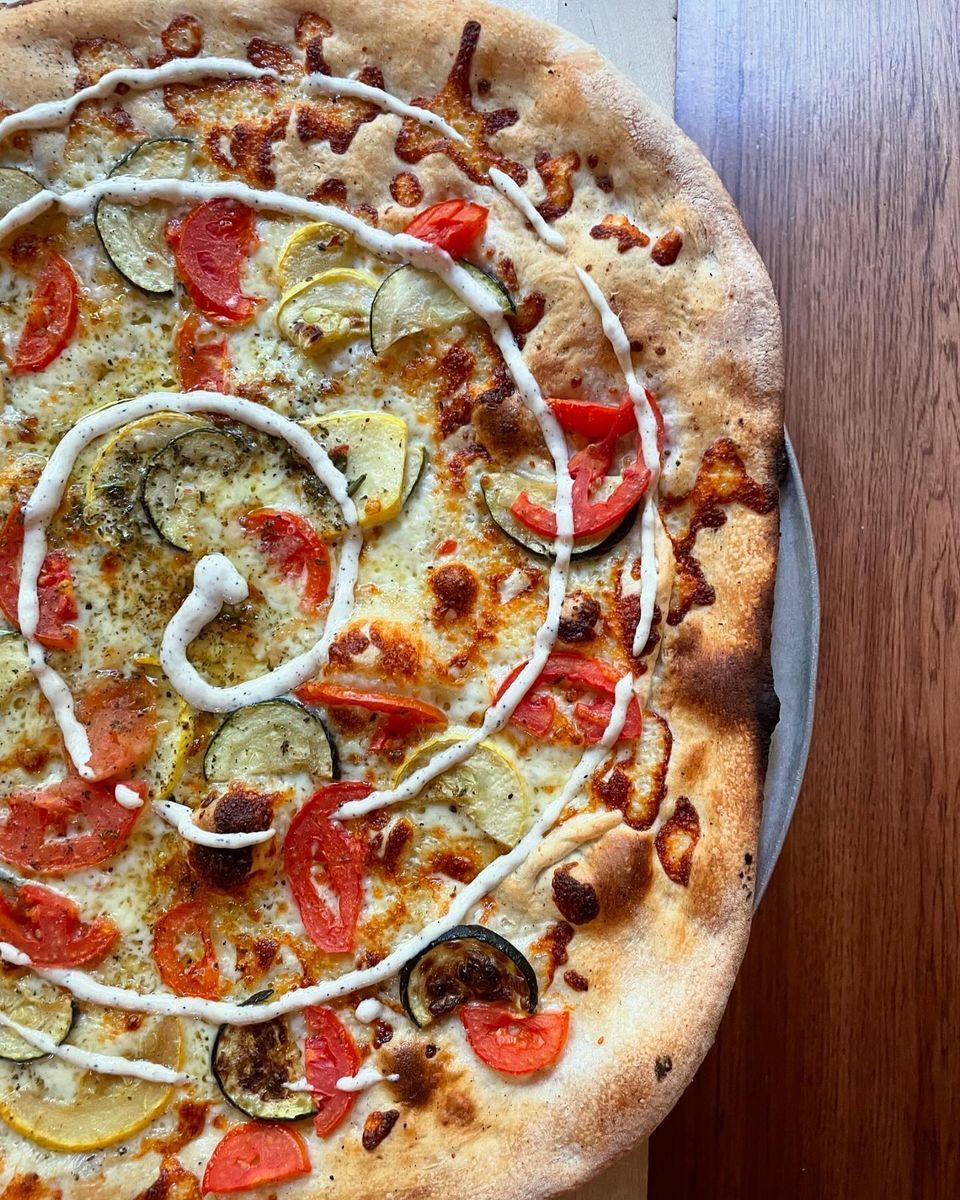 A pizza with tomatoes , zucchini , and cheese on a wooden table.