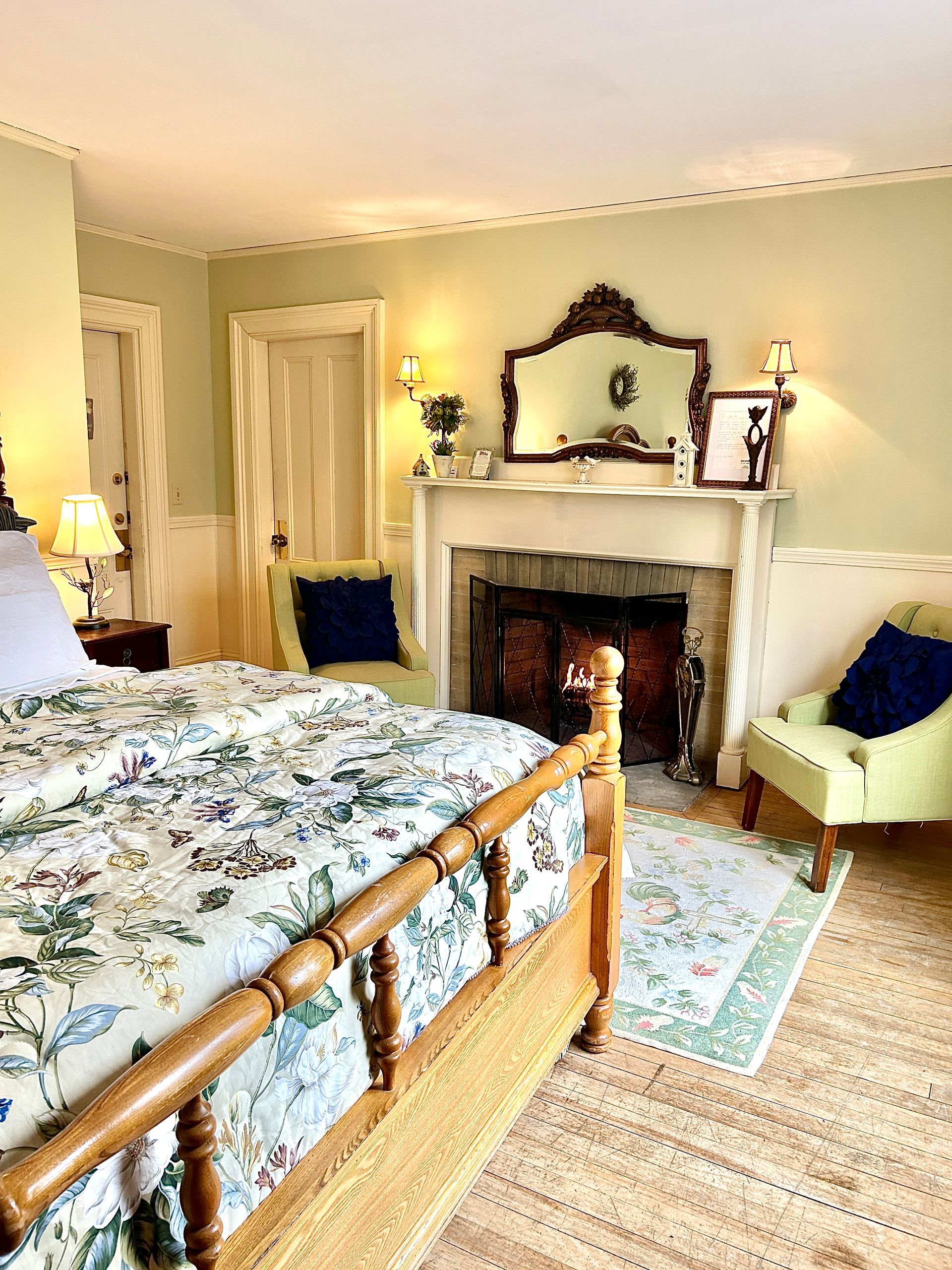 A bedroom with a bed , chair , fireplace and mirror.
