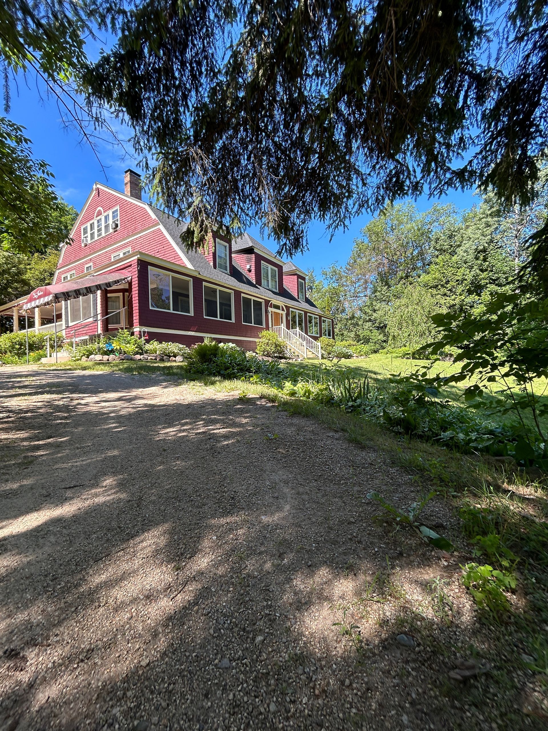 A large red house is surrounded by trees and a gravel driveway.