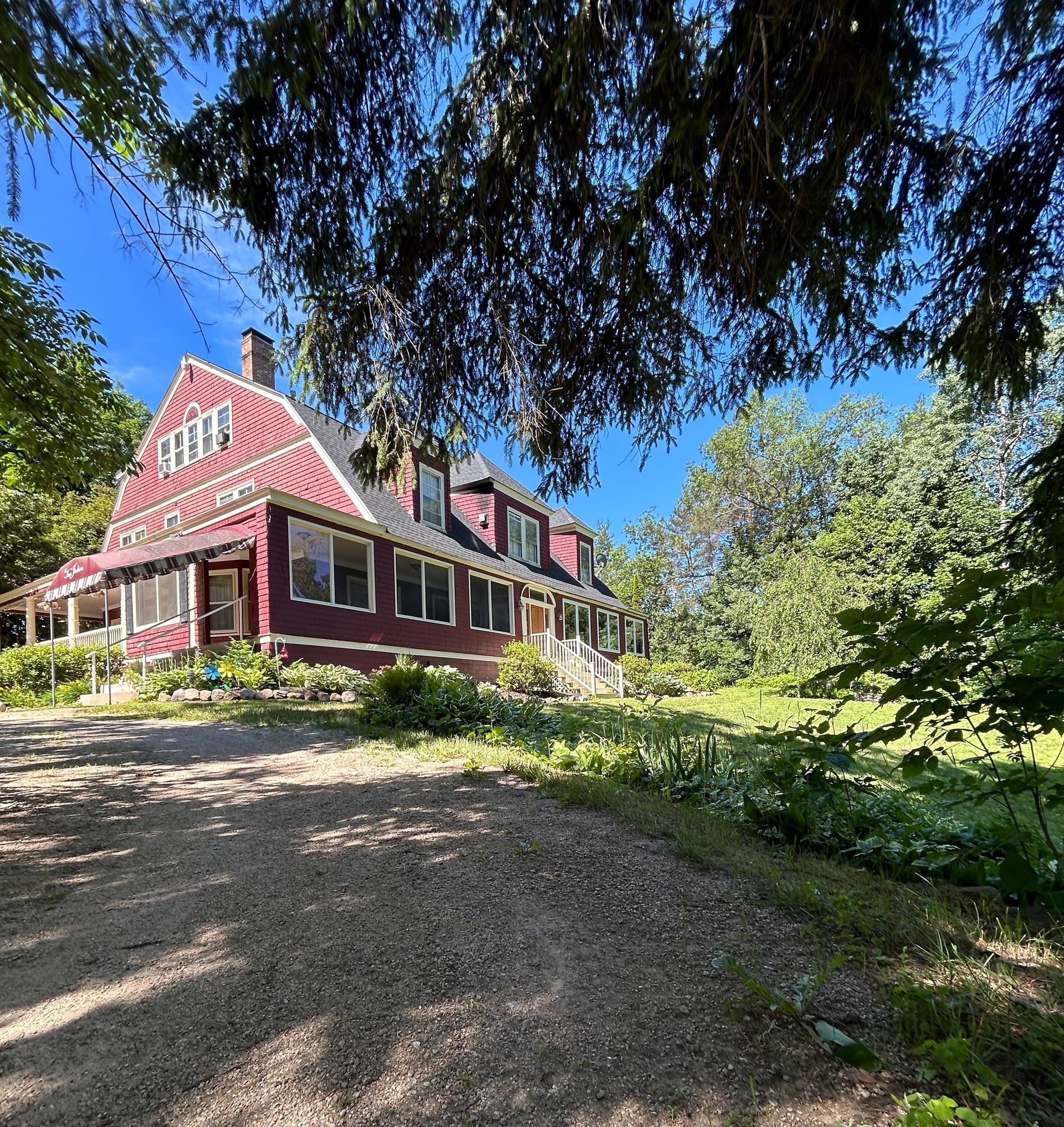 A large red house is surrounded by trees and a dirt road.