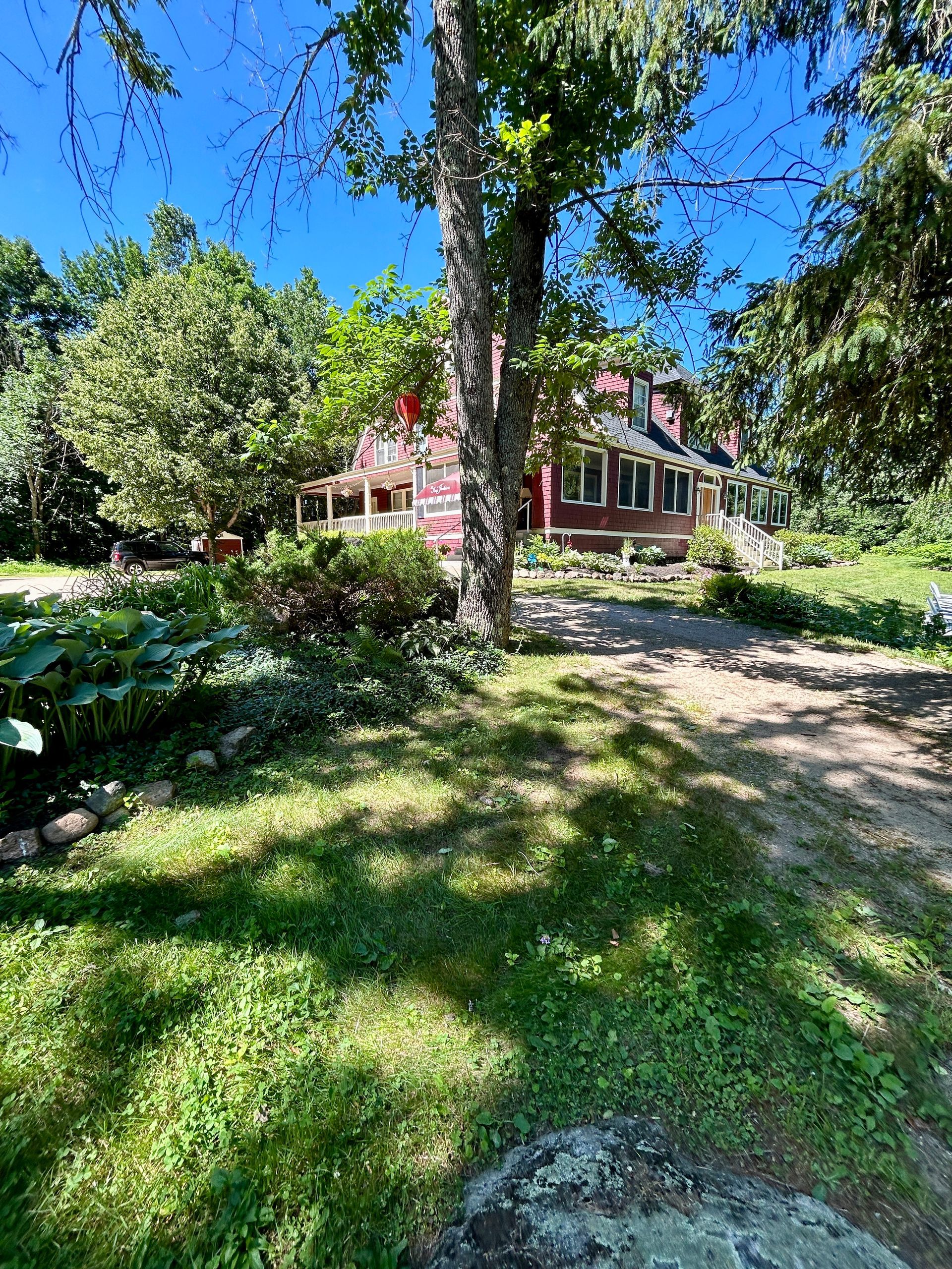 A dirt road leading to a red house surrounded by trees on a sunny day.