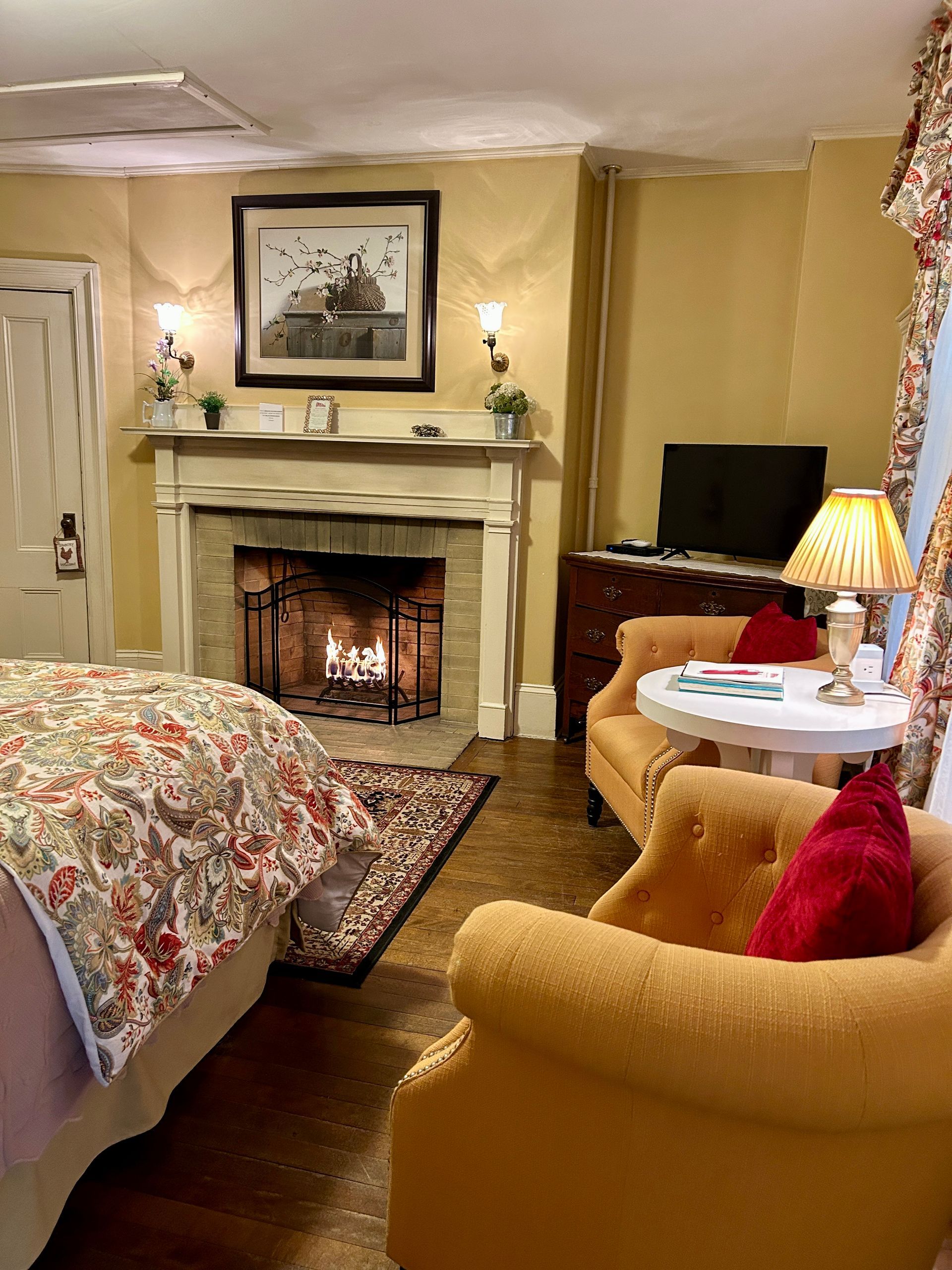 A bedroom with a fireplace , chairs , a table and a television.
