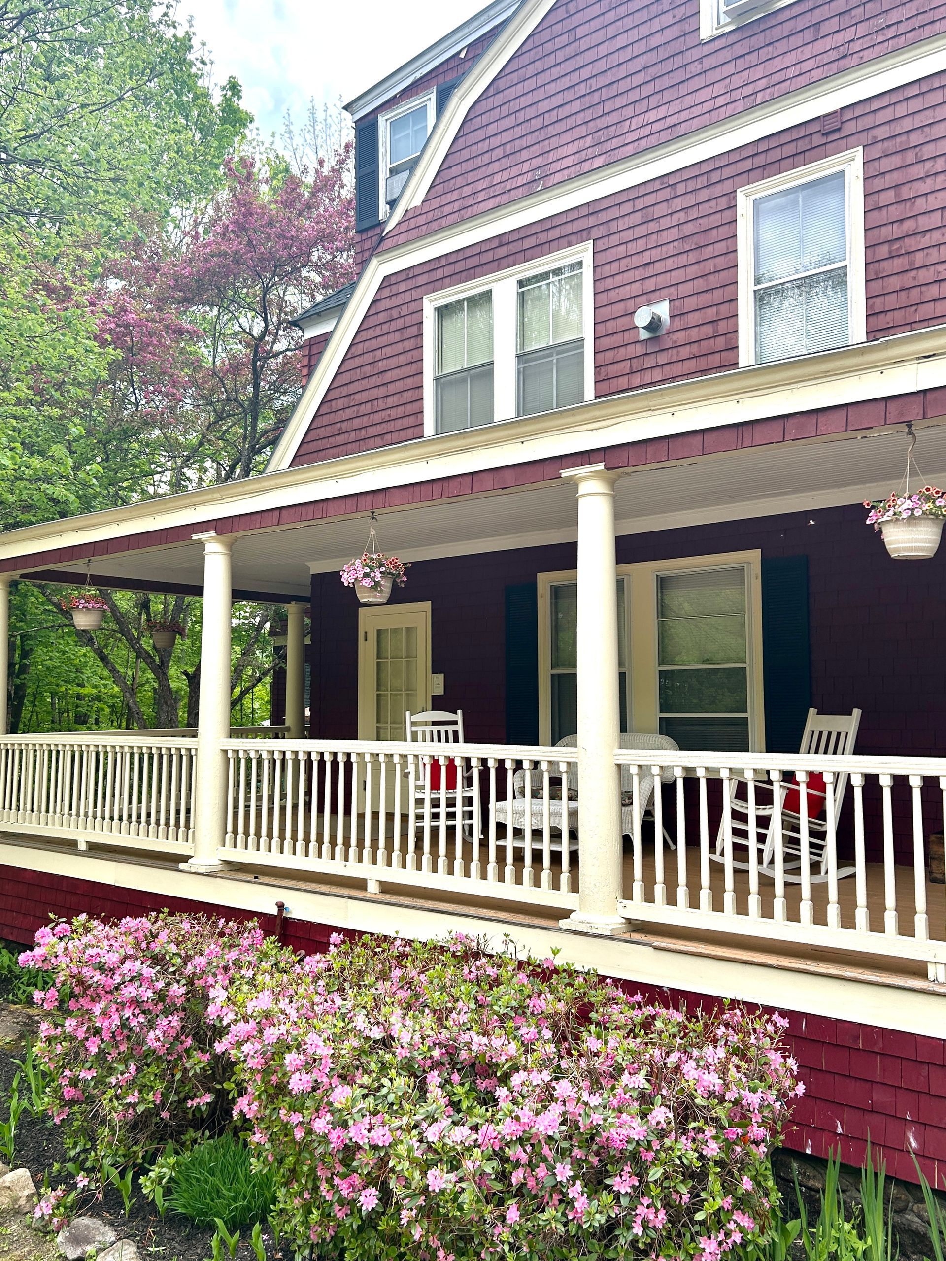 A red house with a porch and flowers in front of it.