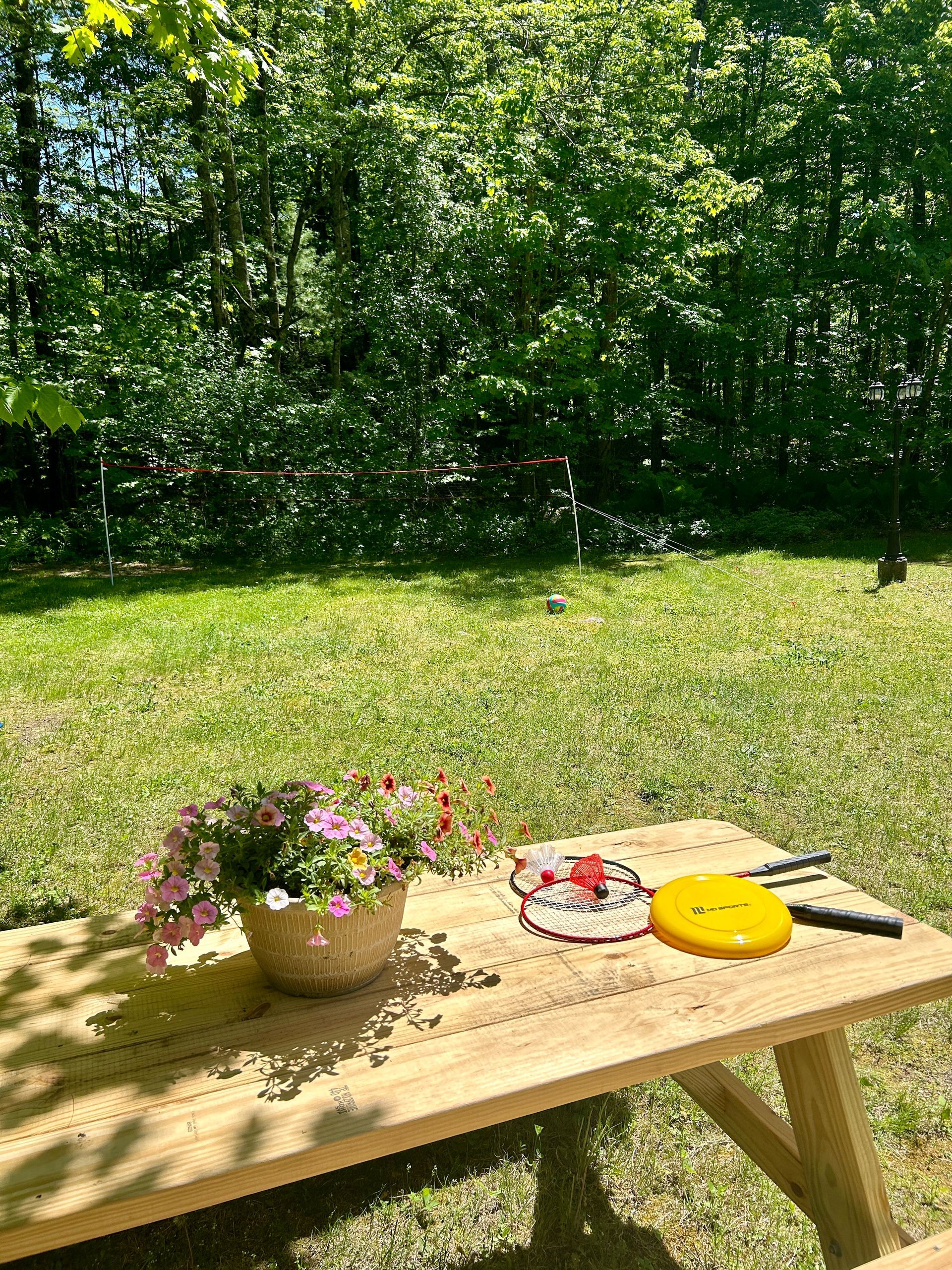 A wooden picnic table with a vase of flowers and frisbees on it.