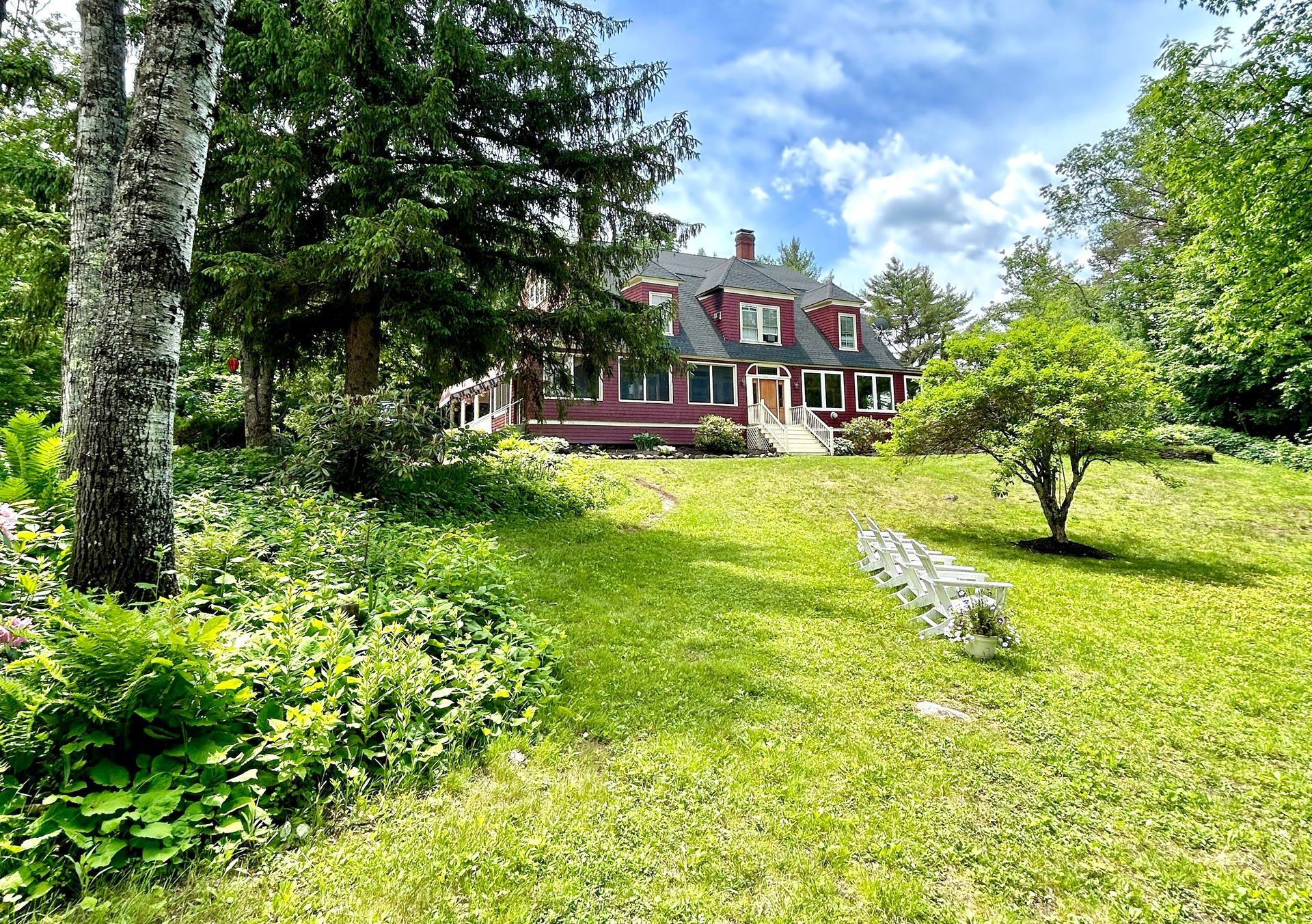 A large house is sitting in the middle of a lush green field surrounded by trees.