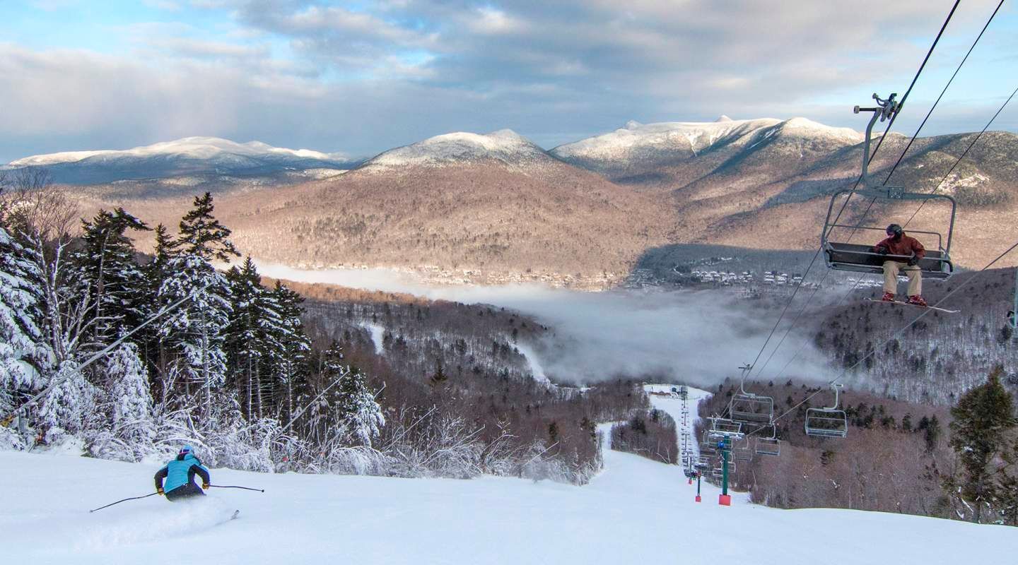 A man is riding a ski lift down a snow covered mountain.