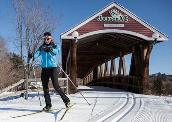 A woman cross country skiing in front of a bridge that says jackson xc