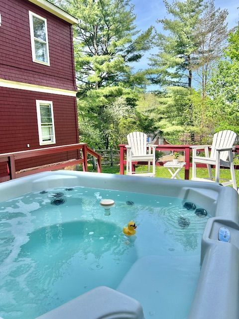 A hot tub with a rubber duck in it is on a deck next to a house.