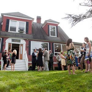 A group of people are standing in front of a large red brick house.