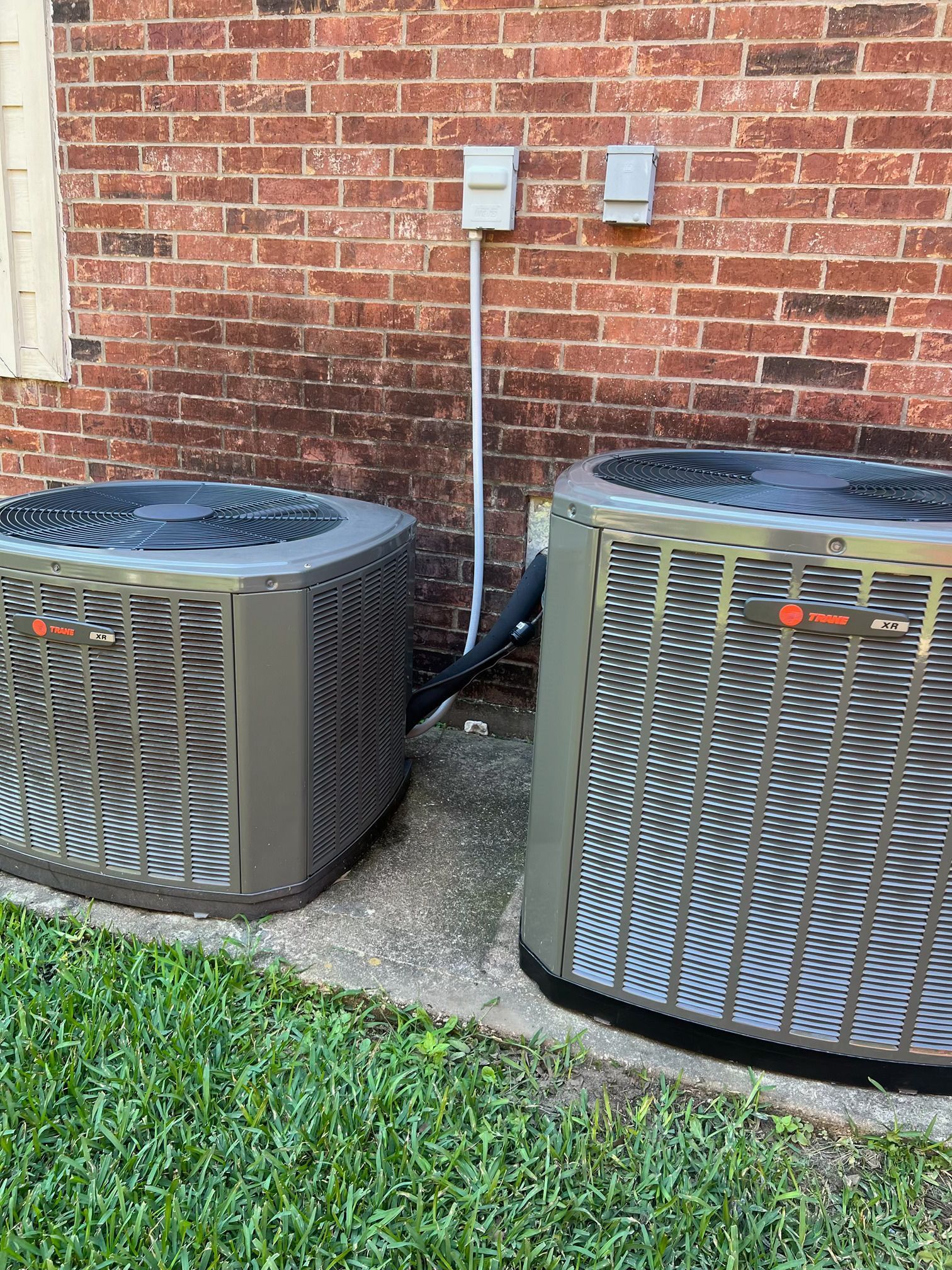 Two air conditioners are sitting next to each other on the side of a brick building.