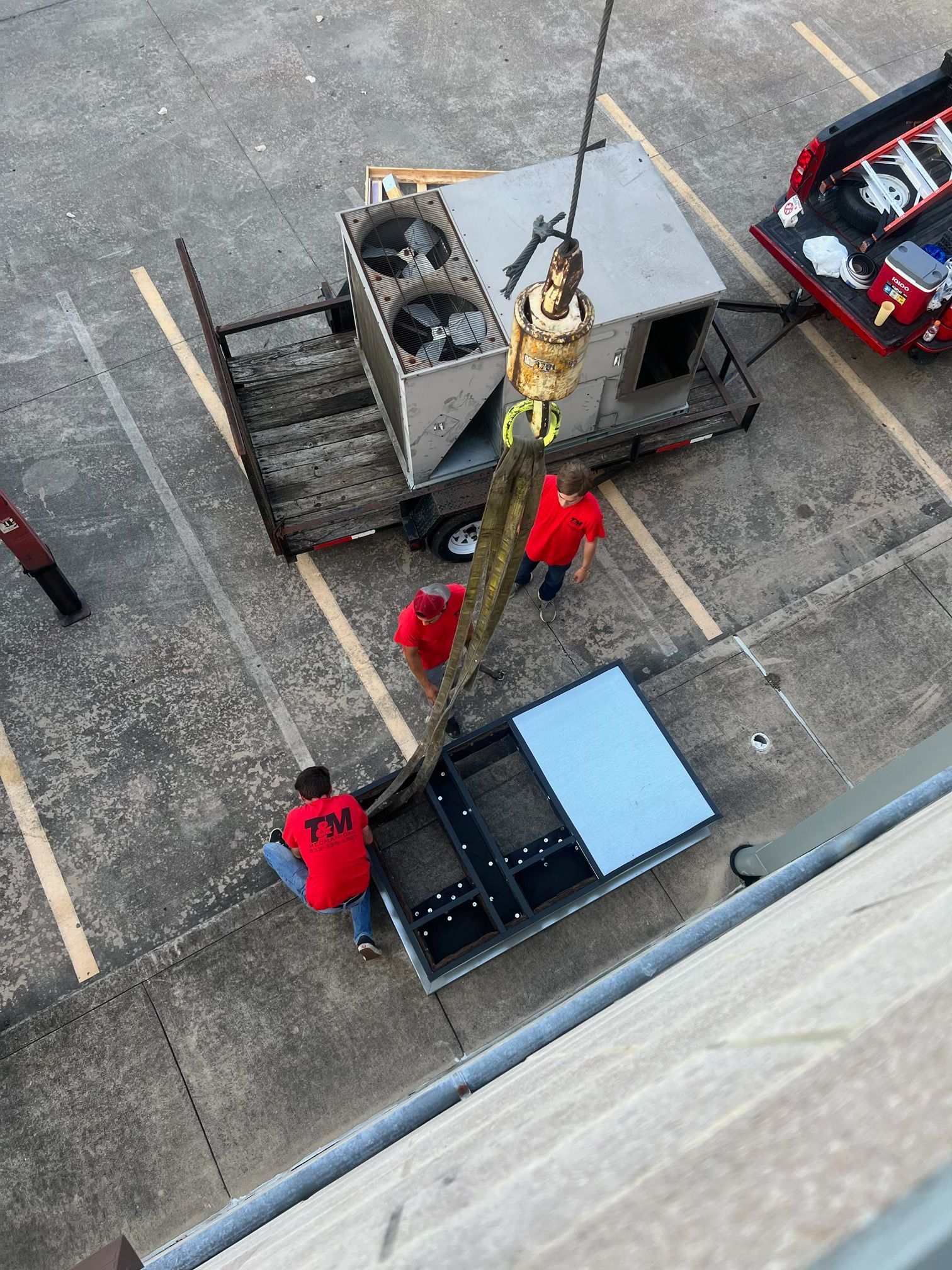 A group of men in red shirts are working on a crane in a parking lot.