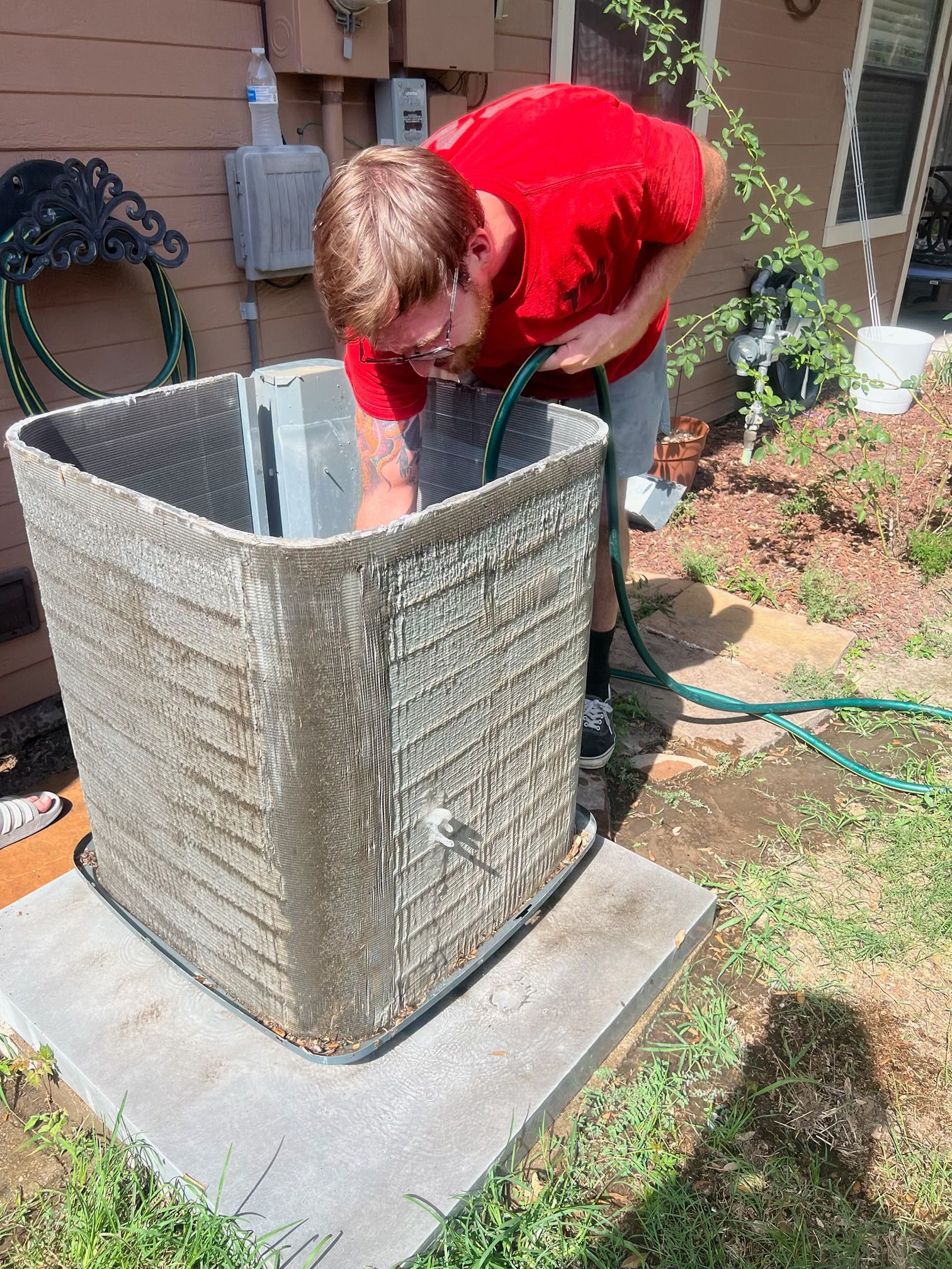 A man is cleaning an air conditioner with a hose.