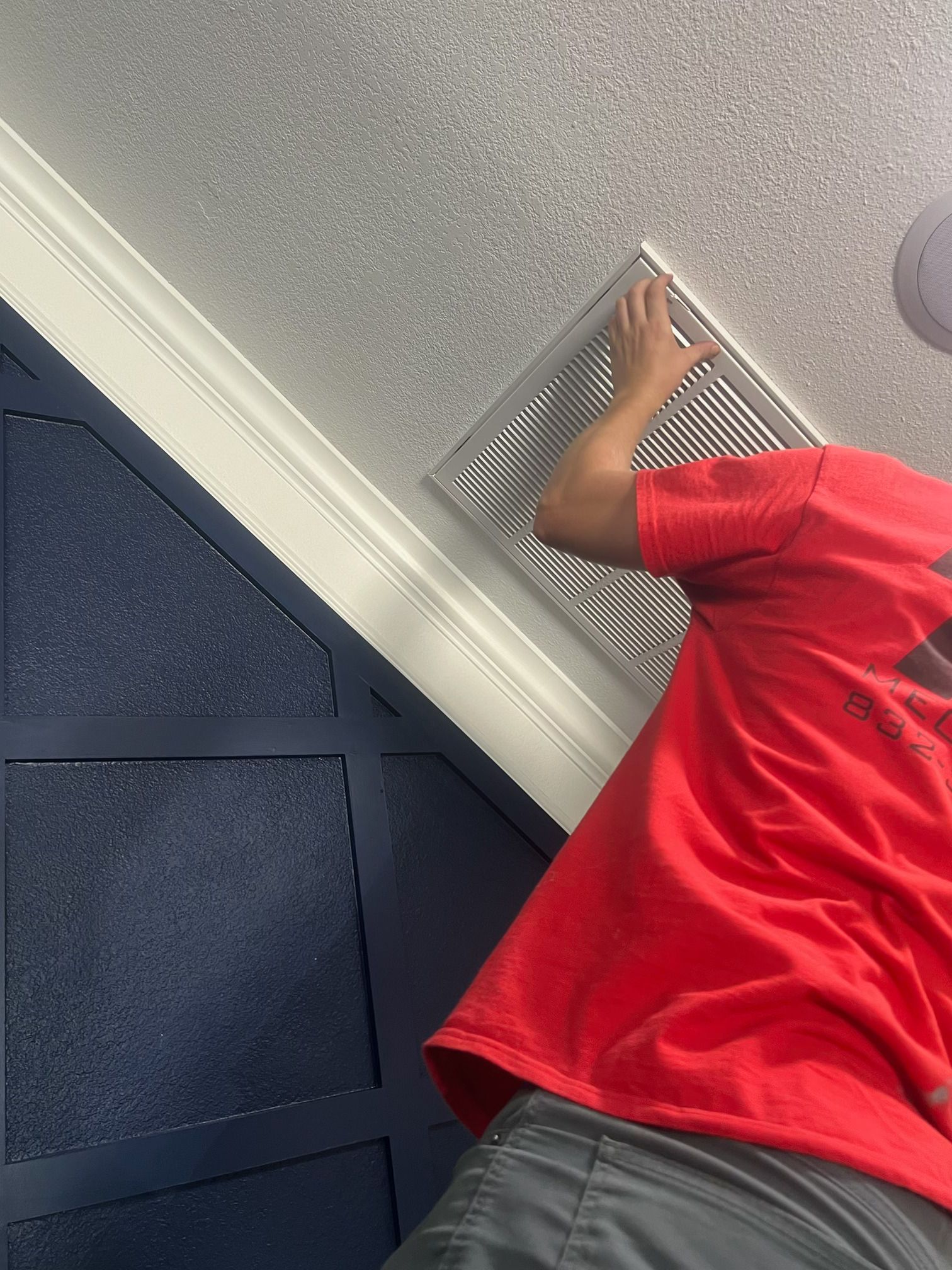 A man in a red shirt is fixing a vent on the ceiling.