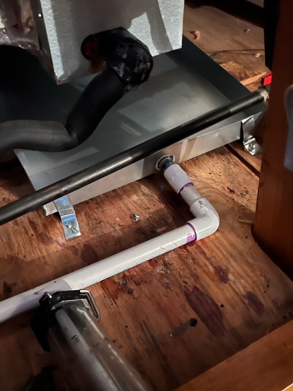 A white pipe is connected to a metal box on a wooden floor